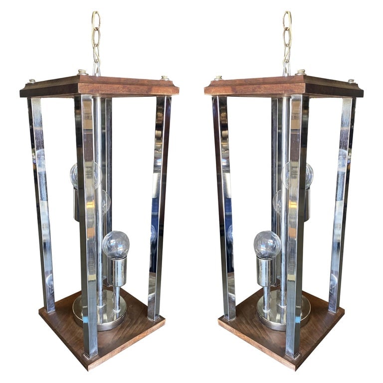 1970s Post Modern Teak and Chrome Pendant Light Fixture, Pair: Original pair of 1970's Brutalist chandeliers with teak tops plates, chrome figures and side bars. Each comes over 36" of gold tone chain for hanging. Reserve: $3,312.00 Shipping: Domestic: Shipping