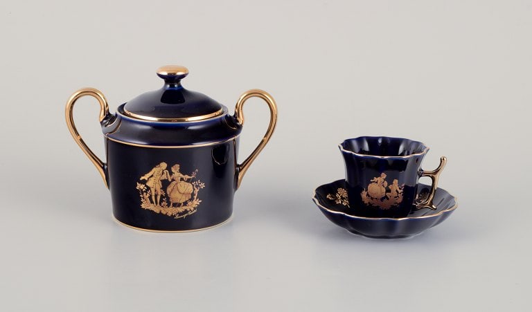 Limoges, France. Two pieces of porcelain consisting of a coffee cup and sugar bowl decorated with: Limoges, France. Two pieces of porcelain consisting of a coffee cup and sugar bowl decorated with 22-karat gold leaf and beautiful royal blue glaze. Sceƒe¨ne galante. Approximately 1970.