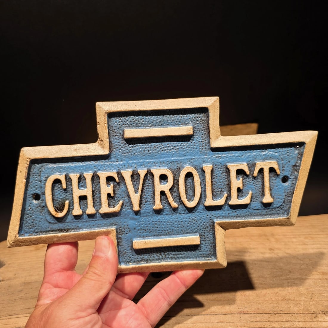 Chevrolet Bowtie Cast Iron Sign Chevy Garage Plaque: Vintage-style cast iron Chevrolet bowtie wall sign with raised lettering, textured blue field, and aged gold-tone border. The design is inspired by early automotive garage, dealership, and service-sta