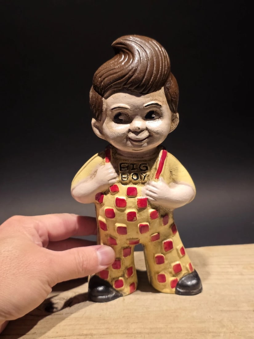 Cast Iron Big Boy Coin Bank: 8 1/2" Tall This reproduction coin bank captures the charm of early 20th-century cast banks with its playful character form and bold, graphic detailing. Featuring a smiling figure dressed in