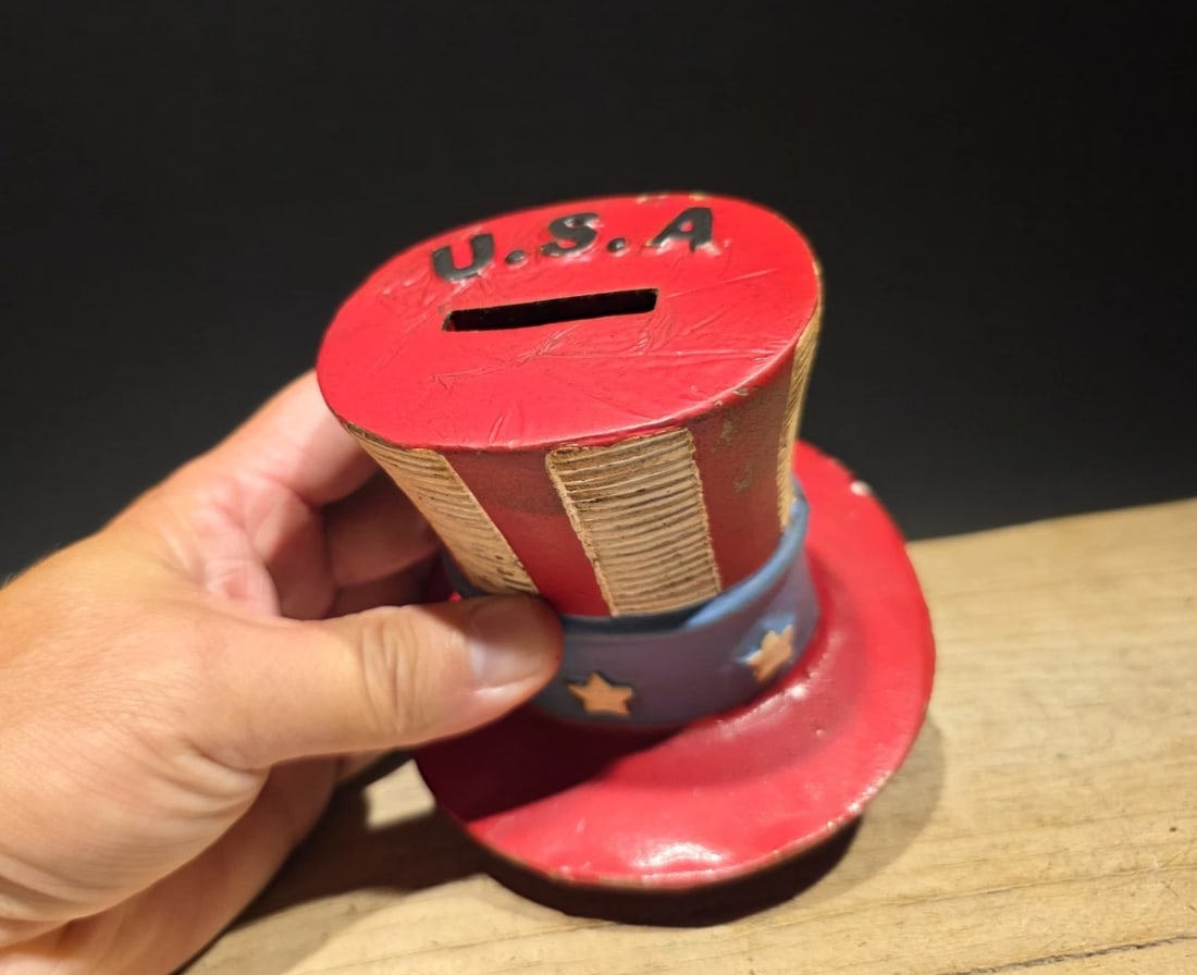 4 1/2" Cast Iron USA Patriotic Hat Coin Bank: 4 1/2" x 4 1/2" Wonderful reproduction Cast Iron USA Patriotic Hat Coin Bank Designed to resemble Uncle Sam's iconic top hat, featuring patriotic red, white, and blue colors with "U.S.A." written on t