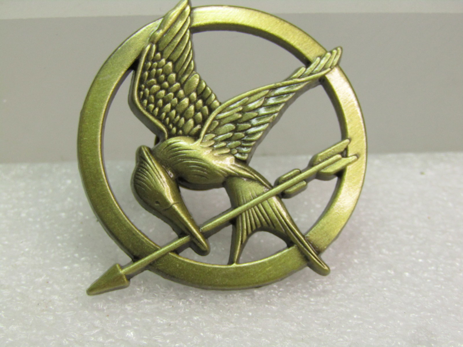Hunger Games Mockingjay Tacck Pin. Signed L.G.F.: Title: Hunger Games Mockingjay Tacck Pin. Signed L.G.F. Description: Hunger Games Mockingjay Tack Pin. Signed L.G.F. Brassy gold tone with circle brooch with the Mockingjay extending slightly beyond