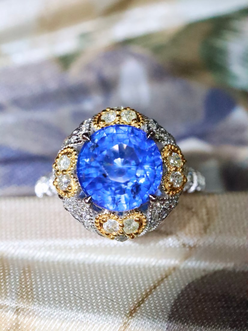 18K Natural Sapphire Ring: Title: 18K Natural Sapphire Ring Description: This sapphire ring showcases a gentle blue that reveals a deep-sea transparency under sunlight. The two-tone gold and silver design, along with the surrou