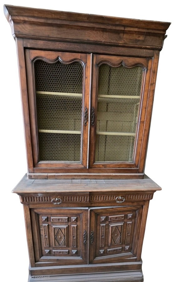 French Provincial Carved Oak Display Cabinet, Early 20th Century: A charming French Provincial two-part display cabinet crafted from oak, likely early 20th century. The upper section features two doors with chicken wire mesh inserts, original ornate metal hardware, 