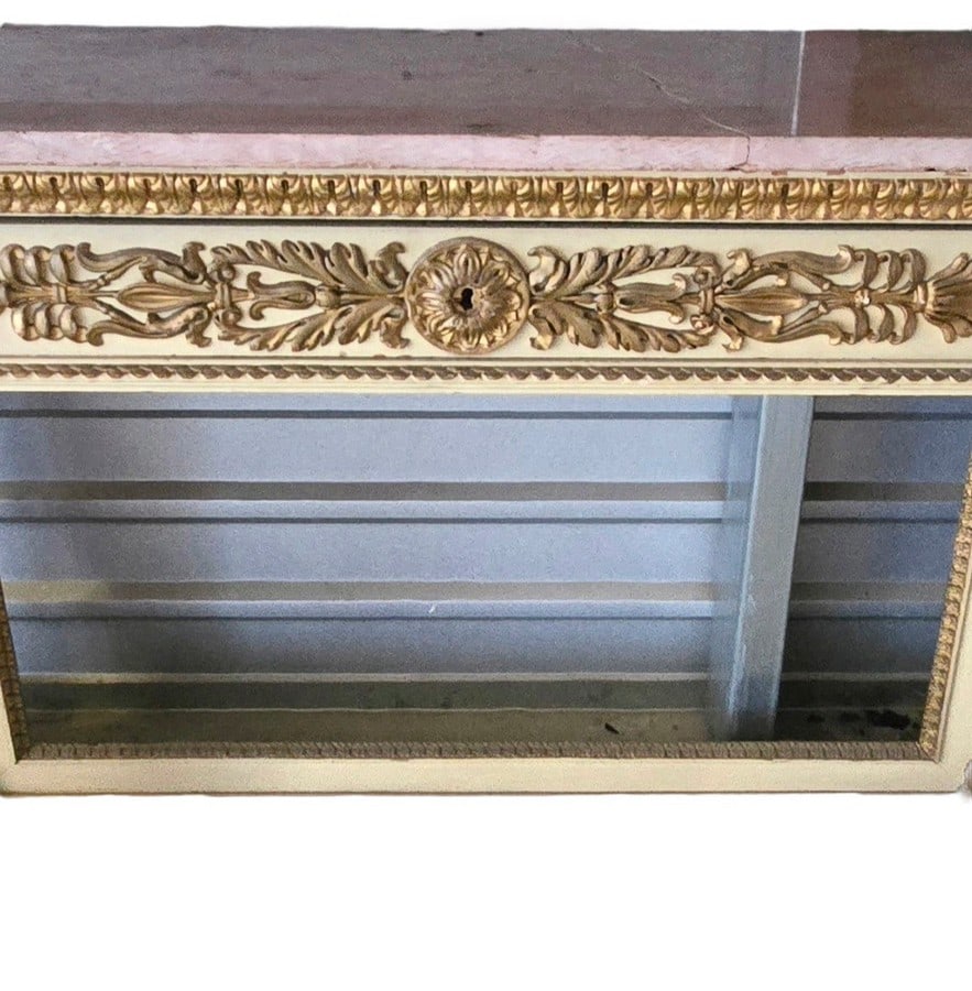 Giltwood and Marble Console Table: A stately console table featuring a rectangular marble top, likely pink or light brown, above an ornate giltwood frieze. The frieze is adorned with classical motifs including acanthus leaves and a cen