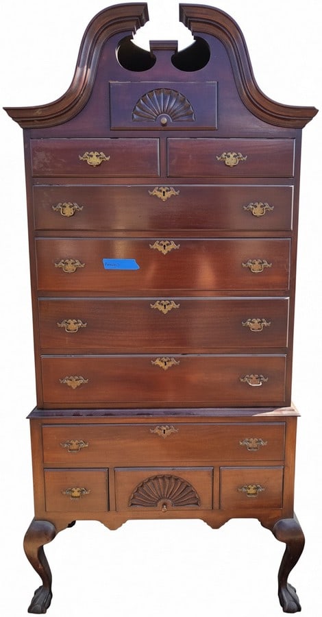 Chippendale Style Carved Mahogany Highboy Chest: A Chippendale style carved mahogany highboy chest, featuring a broken pediment top with flame finials (missing), several drawers with brass pull hardware, and standing on cabriole legs with carved kne