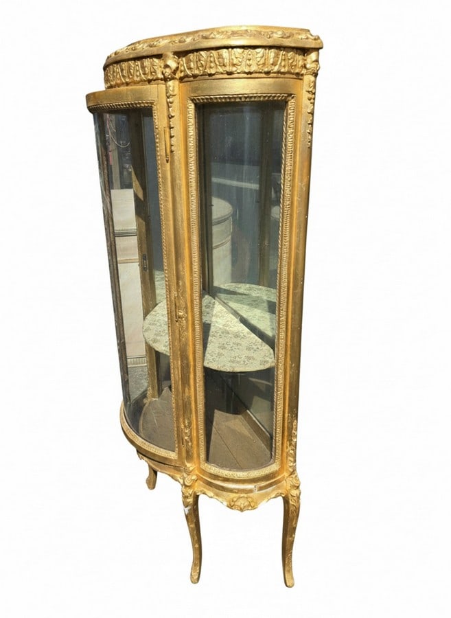 Giltwood Serpentine Curio Cabinet: A serpentine-front curio cabinet, likely Italian, featuring a giltwood finish with ornate carved details throughout. The cabinet has curved glass panels on the front and sides, enclosing two interior 