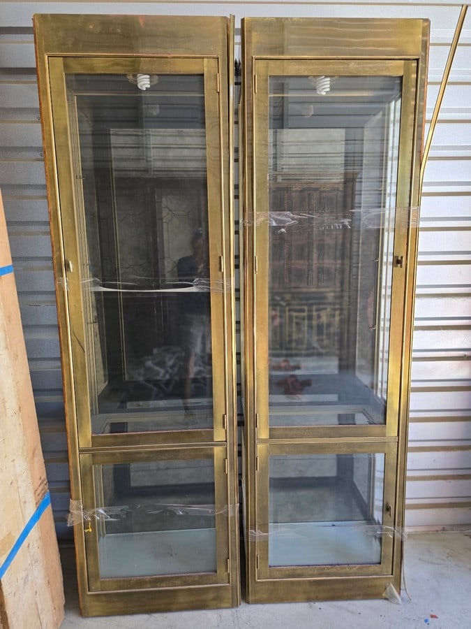 Pair of Brass and Glass Display Cabinets: A pair of tall display cabinets featuring a brass-toned metal frame with glass panels on the front and sides. Each cabinet has interior lighting and multiple glass shelves, making them suitable for