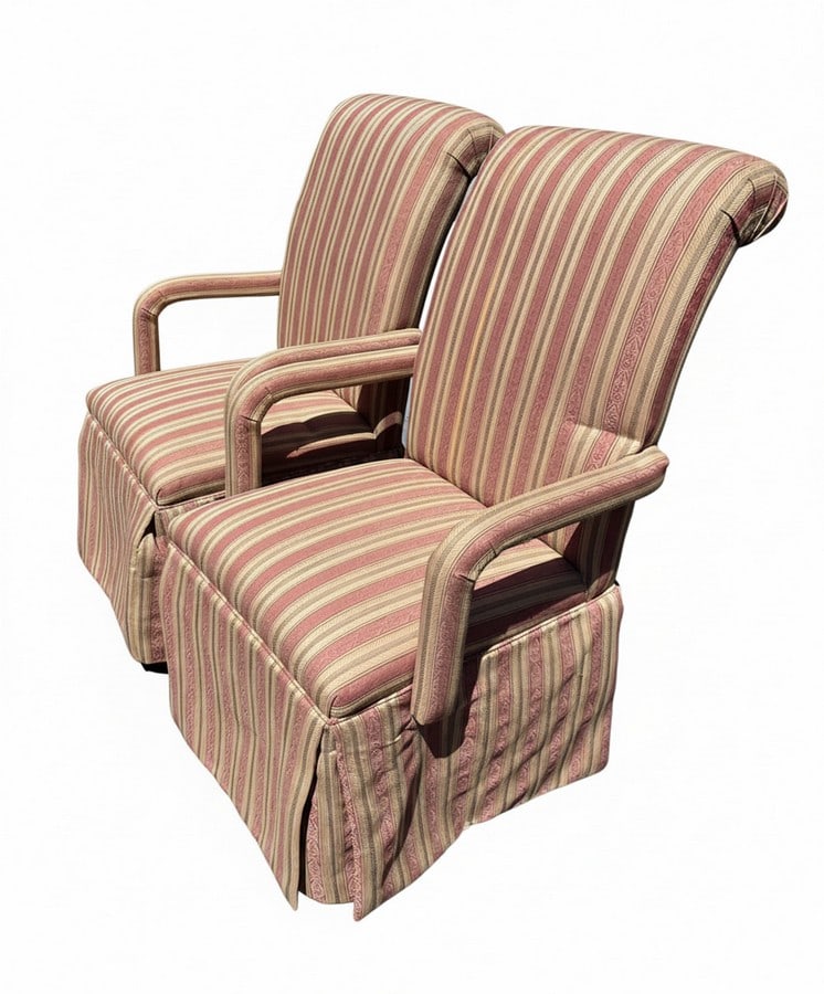 Pair of Upholstered Skirted Armchairs: A pair of armchairs upholstered in a striped fabric with muted red, gold, and green tones. Each chair features a full skirt and rolled arms, suggesting a traditional or classic decor style. The