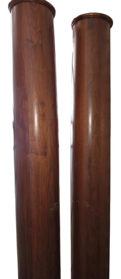 Pair of Hardwood Pedestals: A pair of tall hardwood pedestals, likely walnut or mahogany, with a rich, warm finish. Each pedestal features a simple, elegant cylindrical form with a turned cap and base. They exhibit a classic