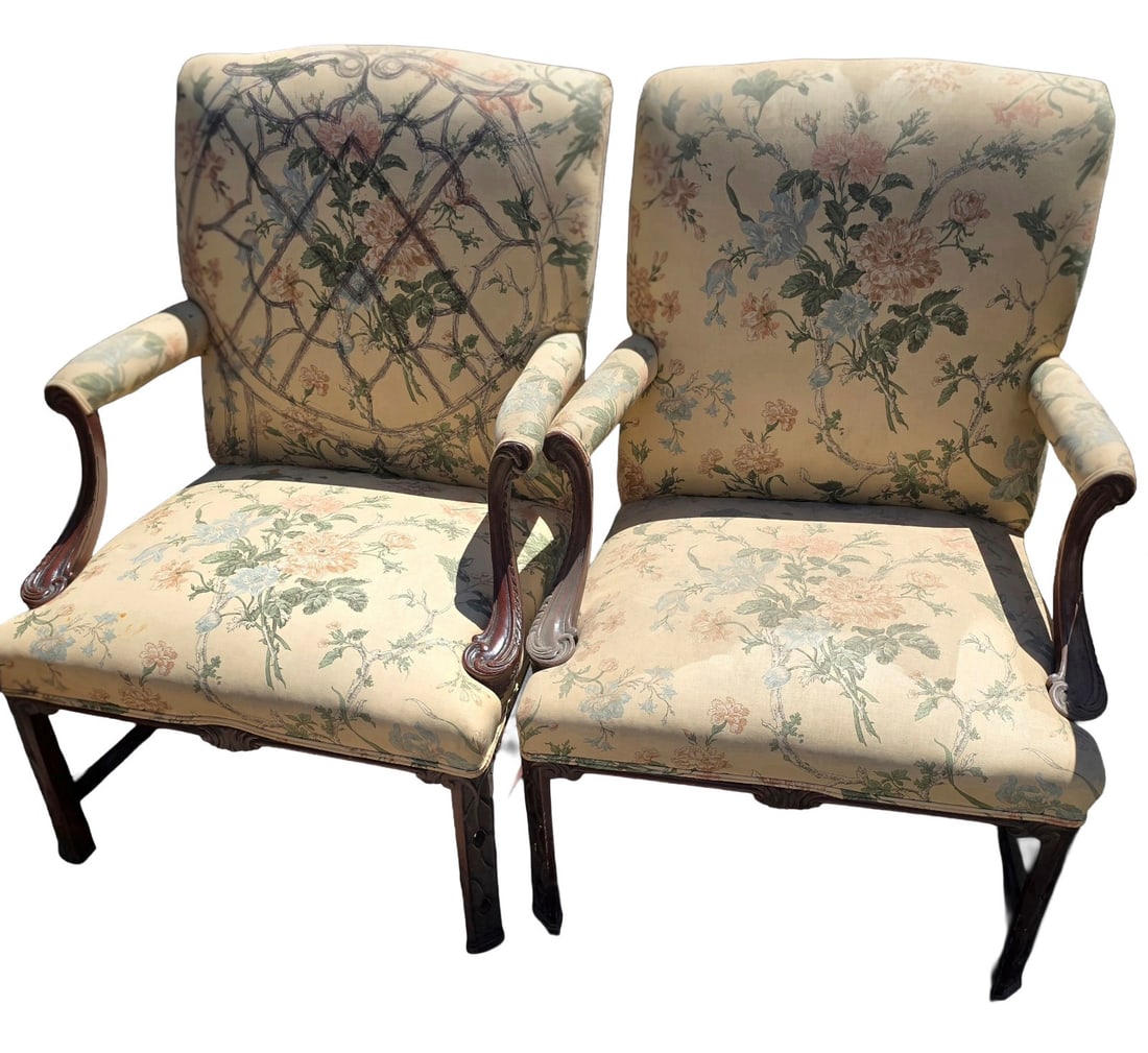 Pair of Carved Wood Armchairs with Floral Upholstery: A pair of traditional armchairs featuring carved wood frames and elegant floral upholstery. The fabric is a light cream color with a pattern of pink, blue, and green flowers and foliage. The wood appe