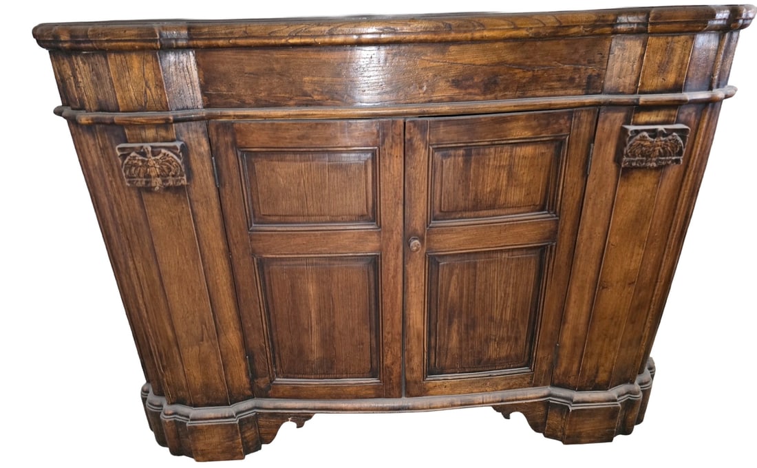 Continental Carved Oak Bombe Commode: This bombe-form commode is crafted from oak, featuring a rich, dark finish. The serpentine front is fitted with two cabinet doors, each with raised panels. Carved eagle motifs adorn the upper