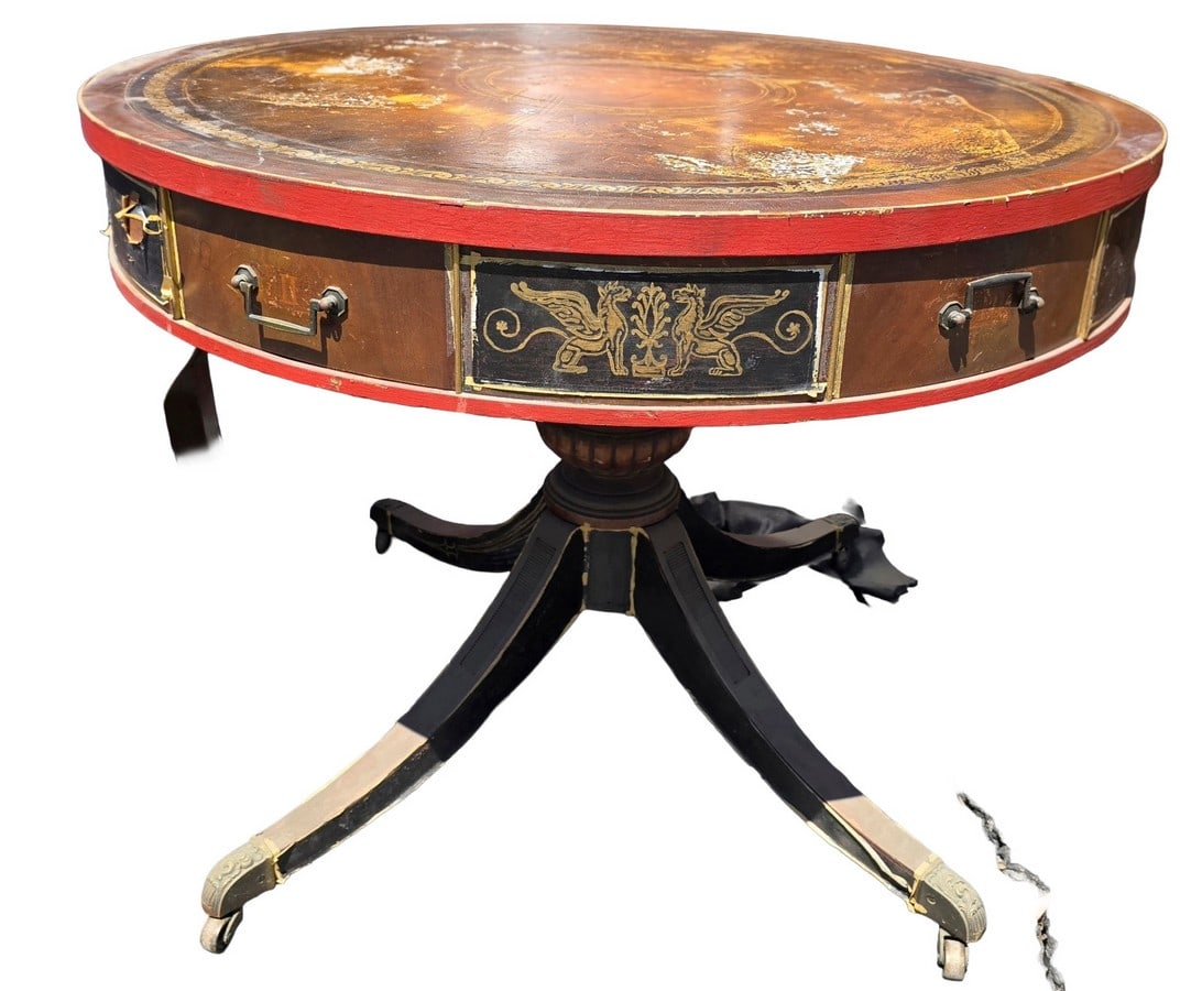 Regency Style Gilt-Tooled Leather Top Drum Table: A Regency-style drum table, likely early 20th century, featuring a circular top with a gilt-tooled leather surface showing significant wear. The apron is fitted with two functional drawers and two dum