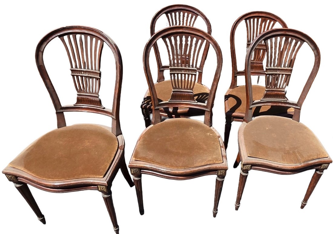 Set of Four Antique Sheraton Style Side Chairs: A set of four antique Sheraton-style side chairs, likely crafted from mahogany or a similar dark wood, featuring carved backrests with vertical splats and ornate detailing. The chairs have upholstered