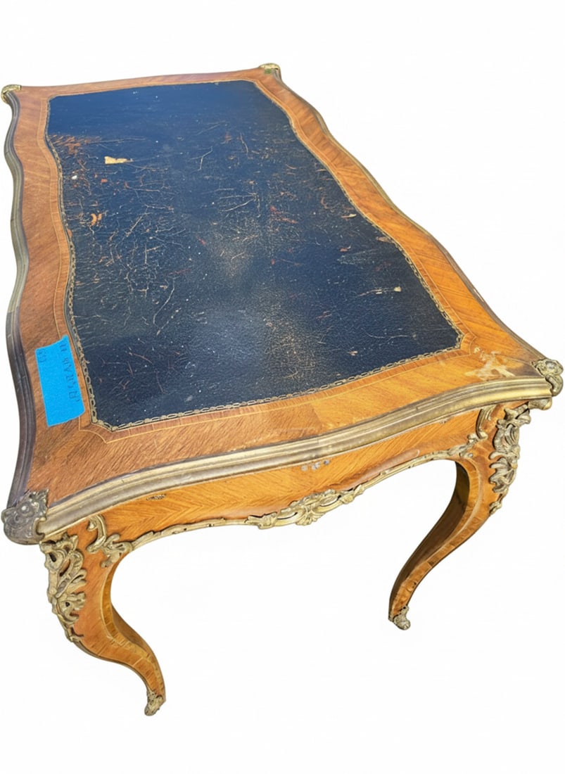 Vintage French Empire Style Inlaid Desk with Tooled Leather Top: A vintage French Empire style desk featuring intricate wood inlay, ornate gilt bronze mounts, and a black tooled leather top with gold accents. The desk has a curvilinear form with three drawers, each