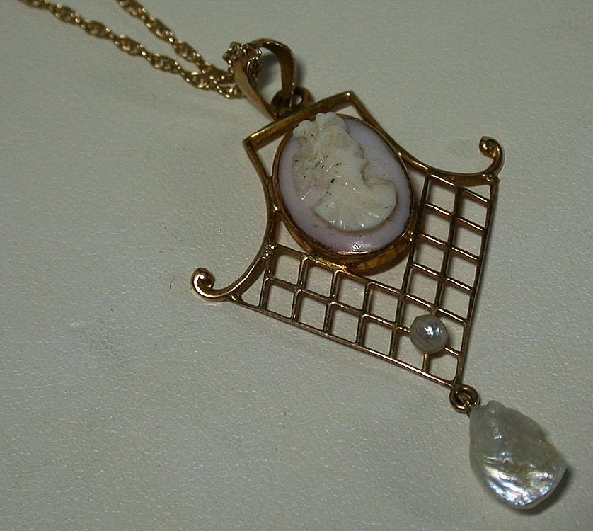 20th C Conch Shell Cameo: Item: 20th C conch shell cameo with 10k gold and pearl accents Provenance: Virginia estate Date: 1891 - 1922 Description: Cameo in the Art Nouveau style with gold latticework and swirls accented with 