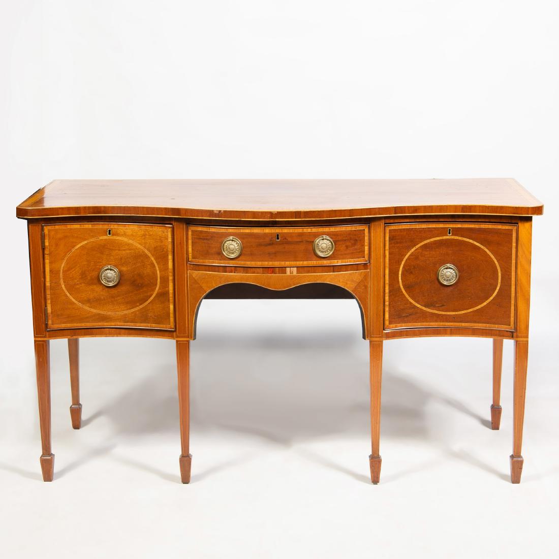 George III Inlaid Mahogany Serpentine-Fronted Sideboard: Fitted with a central drawer flanked by a cupboard door and a drawer. 37 x 66 1/4 x 28 1/4 in.