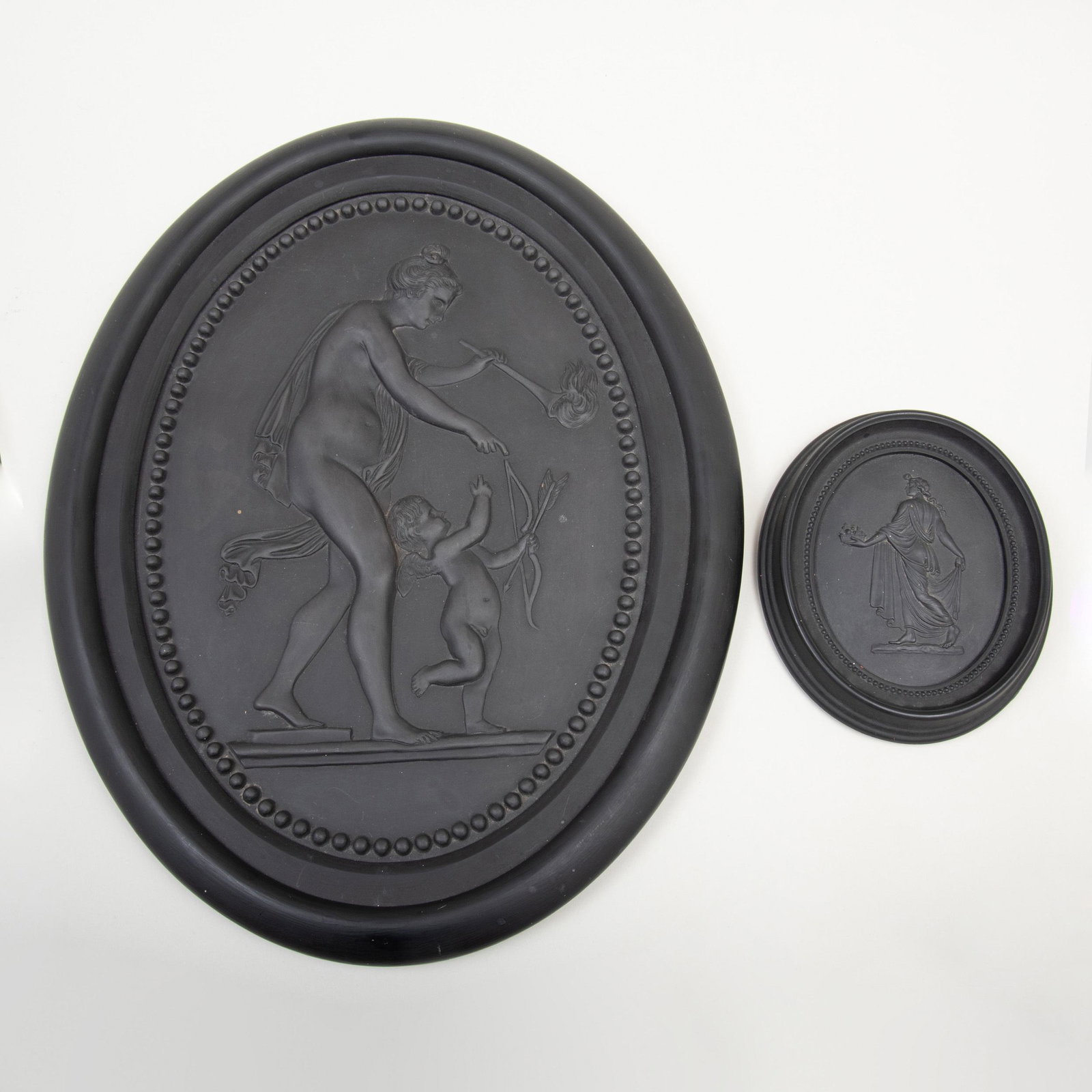 Wedgwood Black Basalt Oval Plaque of Venus and Cupid: Wedgwood Black Basalt Oval Plaque of Venus and Cupid Impressed mark; together with a small Wedgwood oval plaque of a dancing maiden, impressed mark. The larger 17 in. high (frame).