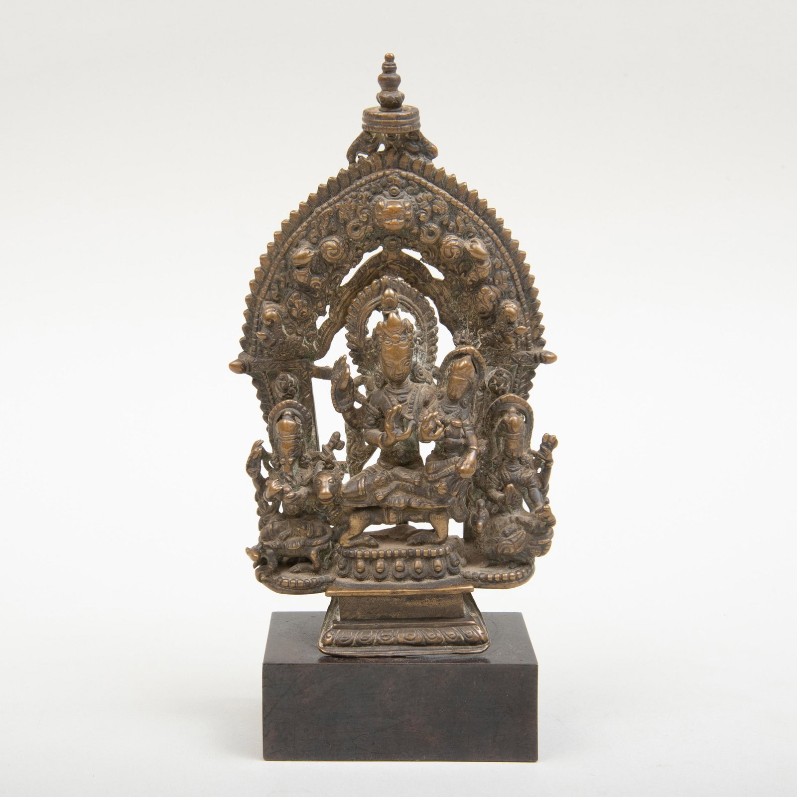 Nepalese Copper Alloy Shrine Depicting Uma-Maheshvara: Nepalese Copper Alloy Shrine Depicting Uma-Maheshvara Shiva seated in lalitasana on a lotus throne on a tiered plinth, his pendant right leg resting upon his bull Nandi, embracing his consort Parvati 