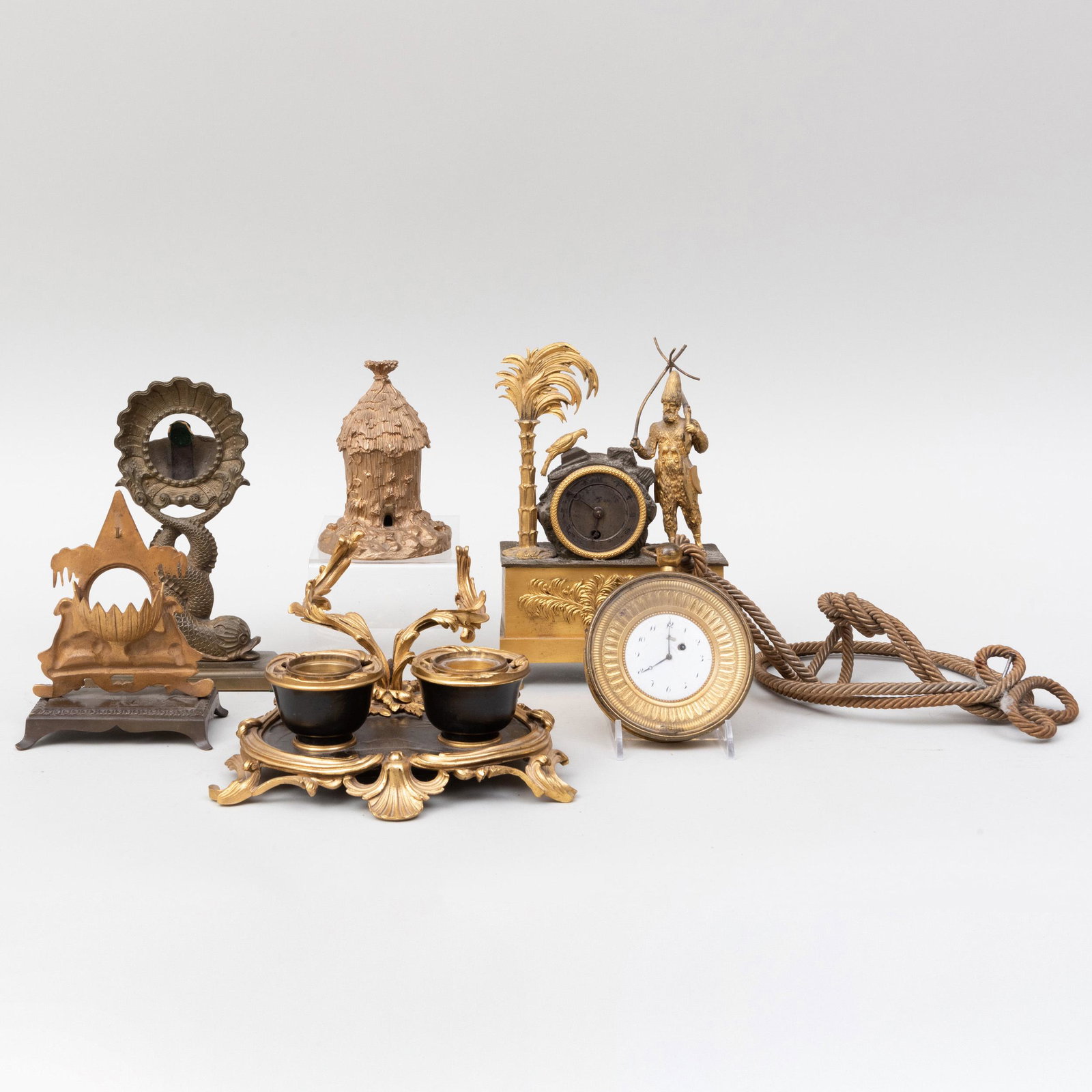 Group of Gilt-Metal-Mounted Clocks and Desk Accessories: Group of Gilt-Metal-Mounted Clocks and Desk Accessories Comprising: A clock mounted with an exotic figure A circular clock marked 'Caillor, Paris' A pocket watch holder on dolphin supports A pyramid p