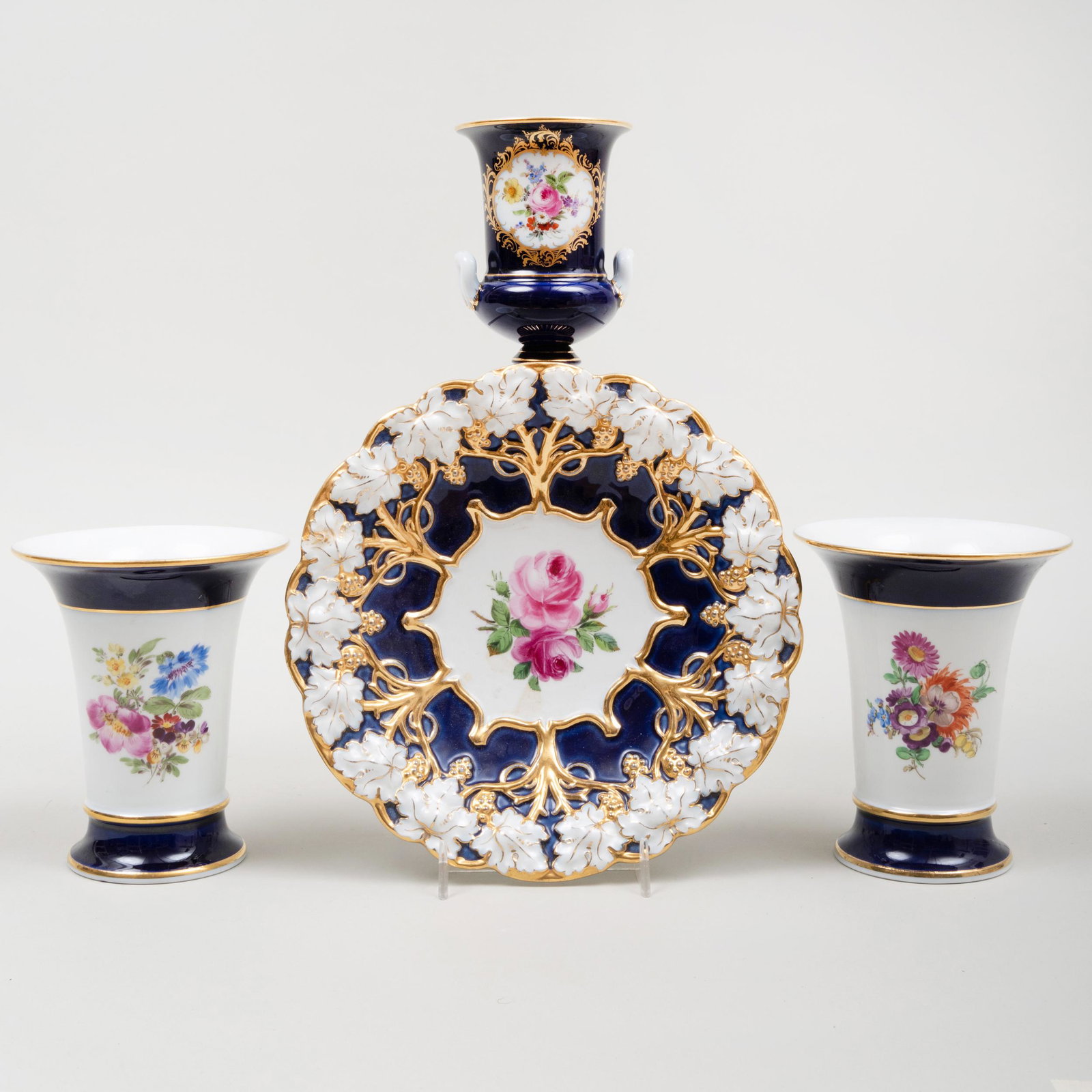 Group of Meissen Cobalt Ground Porcelain Wares: Group of Meissen Cobalt Ground Porcelain Wares Each with blue crossed swords, incised and impressed numbers. Comprising: A pair flaring conical vases A small campagna form vase A dish decorated with r