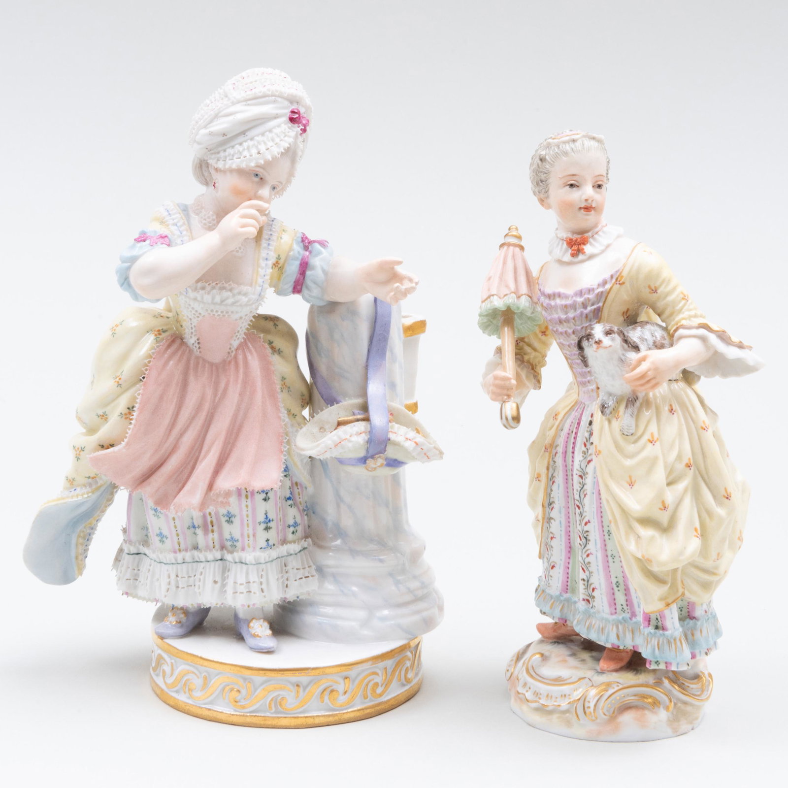 Two Meissen Figures of Maidens: Two Meissen Figures of Maidens Each with blue crossed swords and incised numbers; the first with cupids arrows, the second with a puppy and a parasol. The first 6 1/4 in. high, the second 5 3/4 in. hi