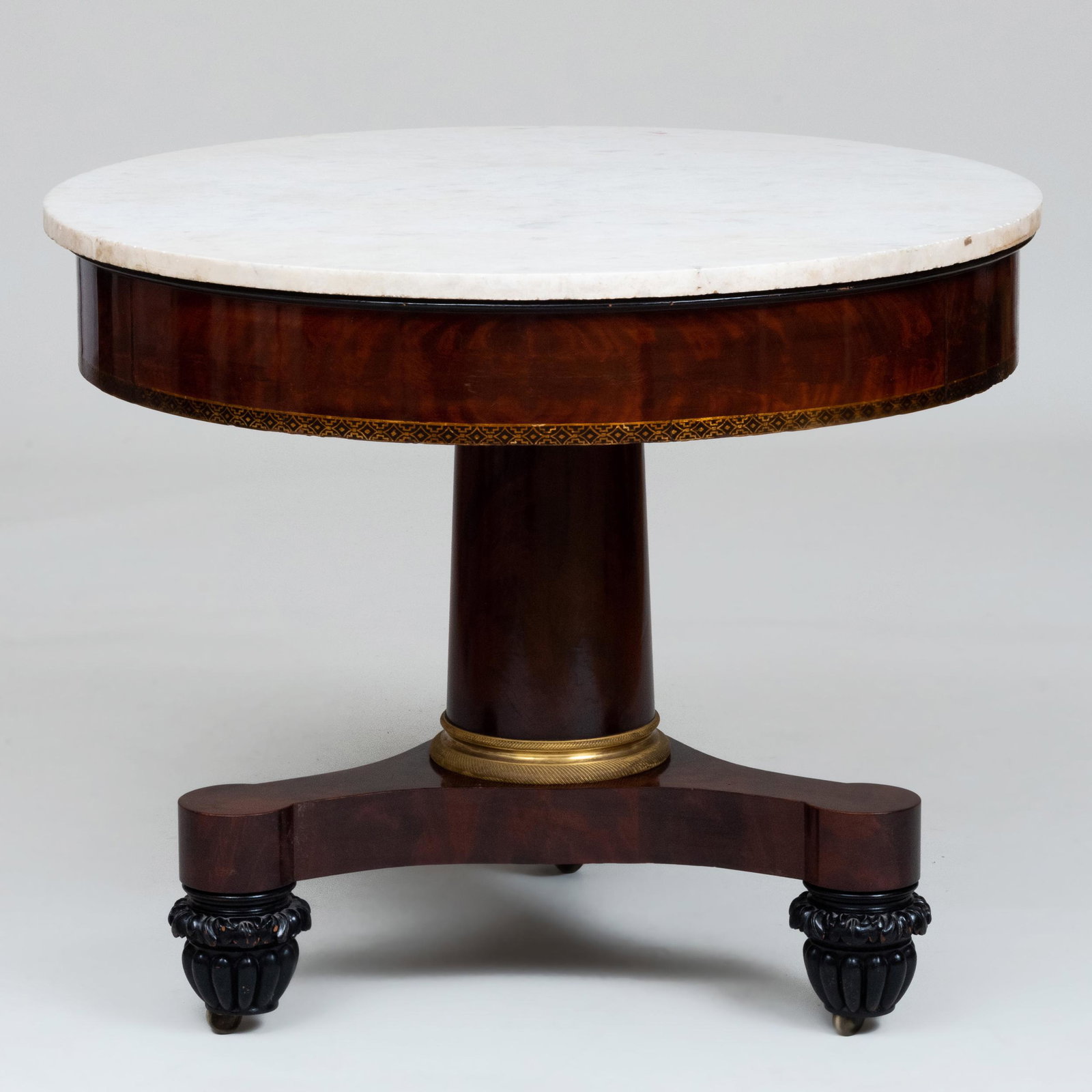 American Classical Mahogany, Ebonized and Stenciled: American Classical Mahogany, Ebonized and Stenciled Center Table Fitted with a white marble top and a gilt-bronze collar on the base, raised on casters. 30 x 36 1/2 in. diam.