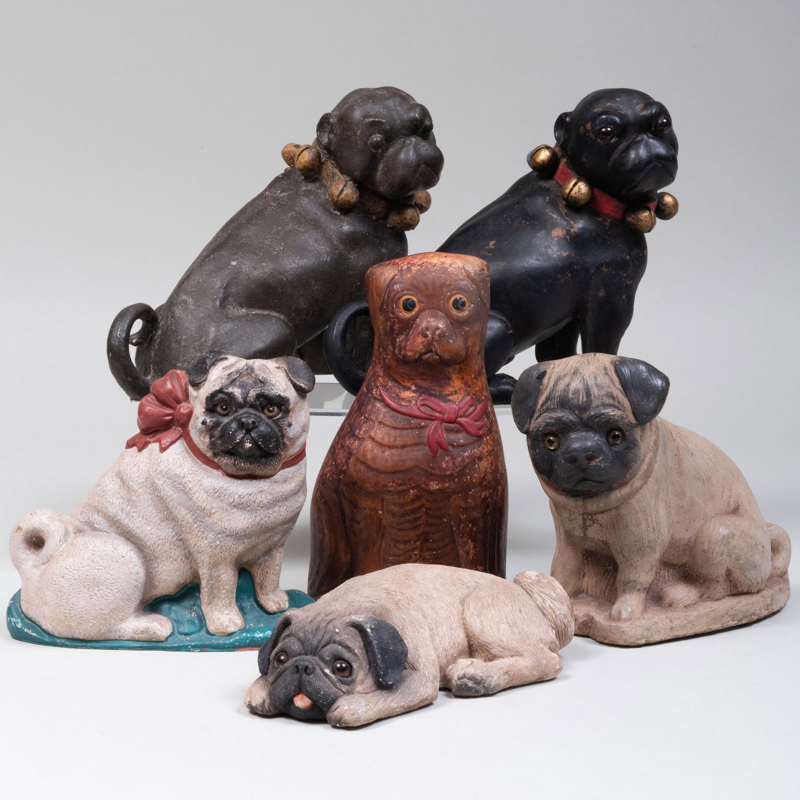 Group of Six Pug Form Doorstops: Group of Six Pug Form Doorstops Comprising: A folk art painted plaster example A Sandicast recumbant example inset with glass eyes A Department 56 painted cast iron example A painted concrete example