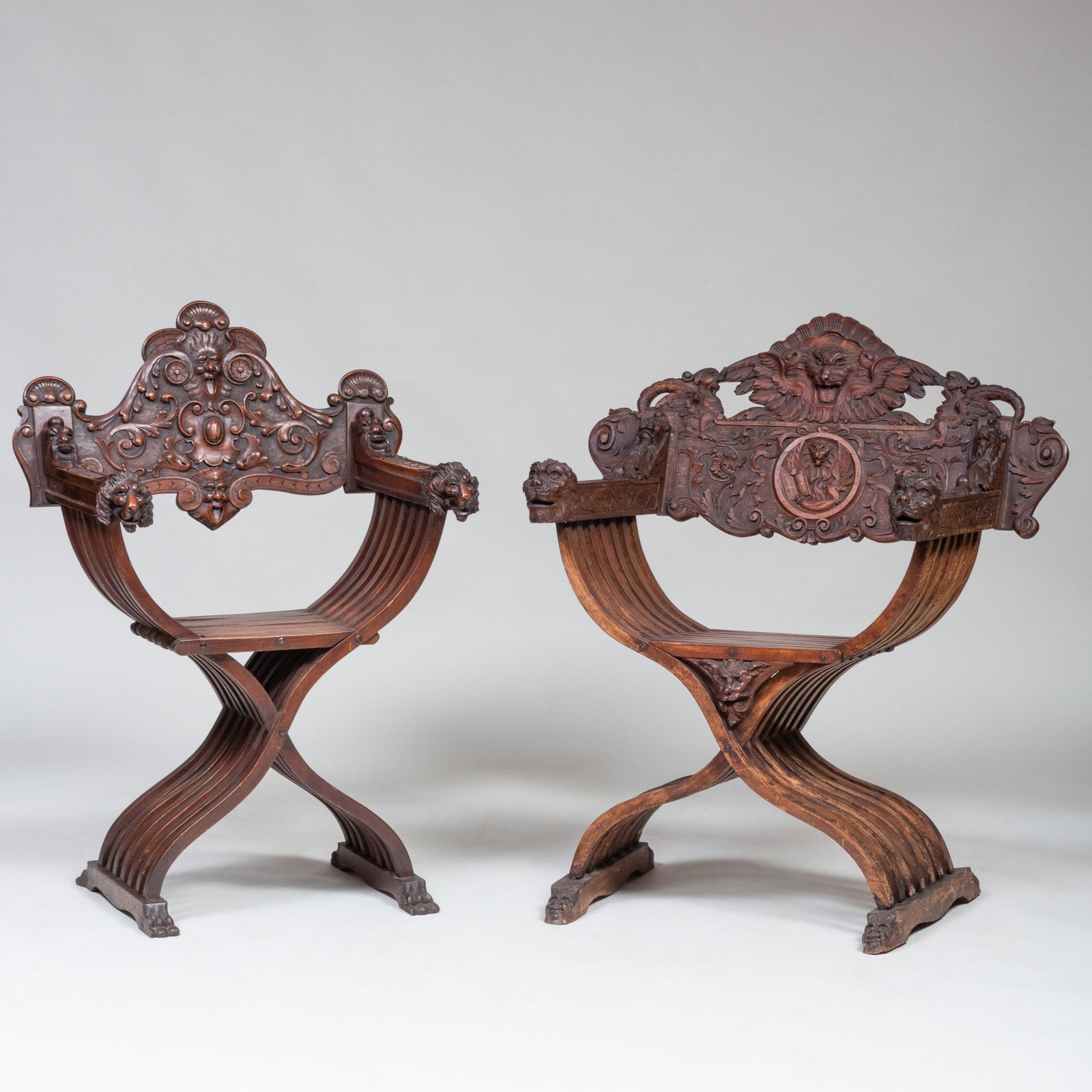 Two Italian Carved Walnut Savonarola Chairs: Two Italian Carved Walnut Savonarola Chairs Each with back carved with mask and arms ending in lion head terminals. The first 39 x 33 x 19 in., height of seat 18 1/2 in.; the second 39 1/2 x 28 x 17 i