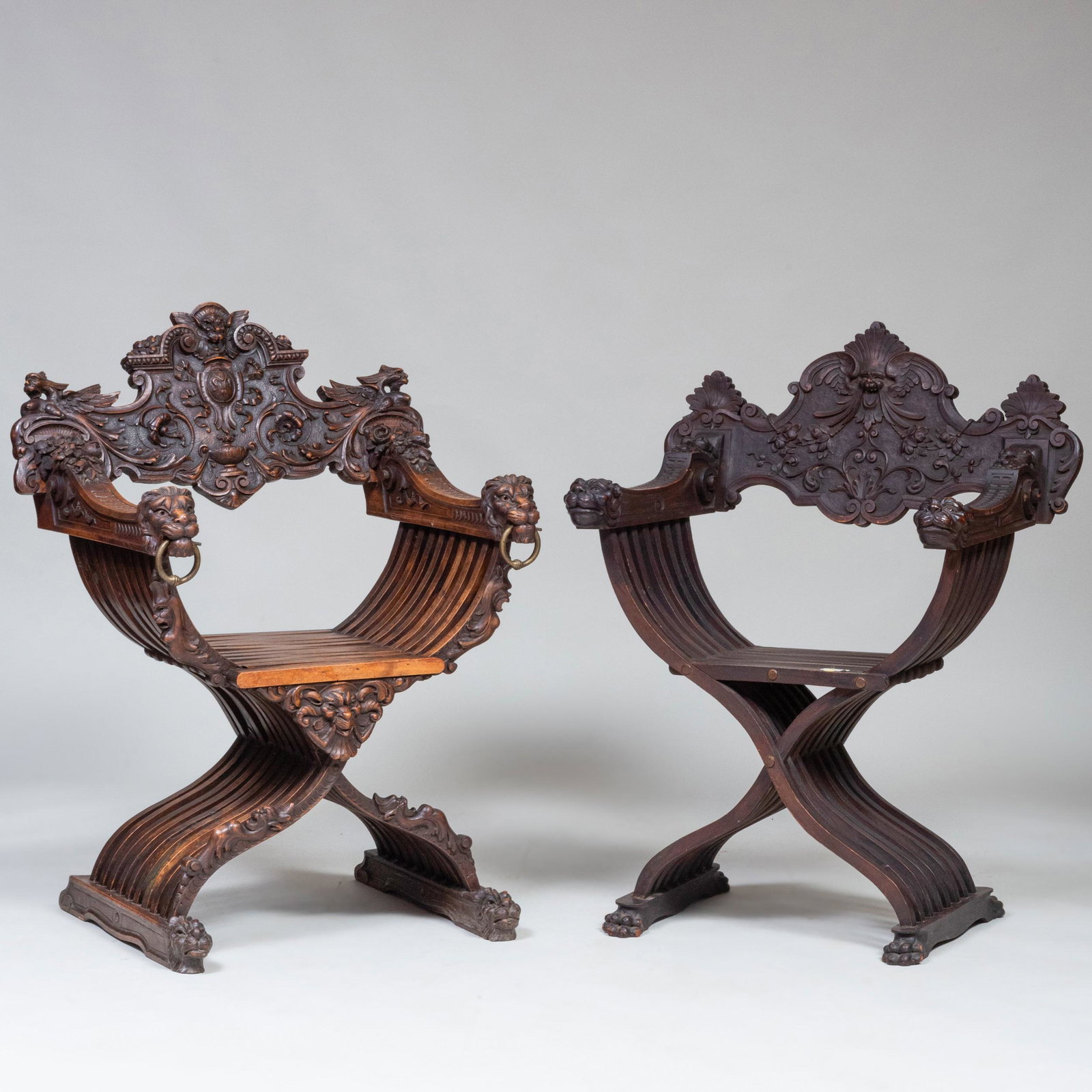 Two Italian Carved Walnut Savonarola Chairs: Two Italian Carved Walnut Savonarola Chairs Both with arms carved with bouquets ending in lion head terminals. The first 39 x 30 1/2 x 19 in., height of seat 17 1/2 in.; the second 41 x 30 x 19 in., h