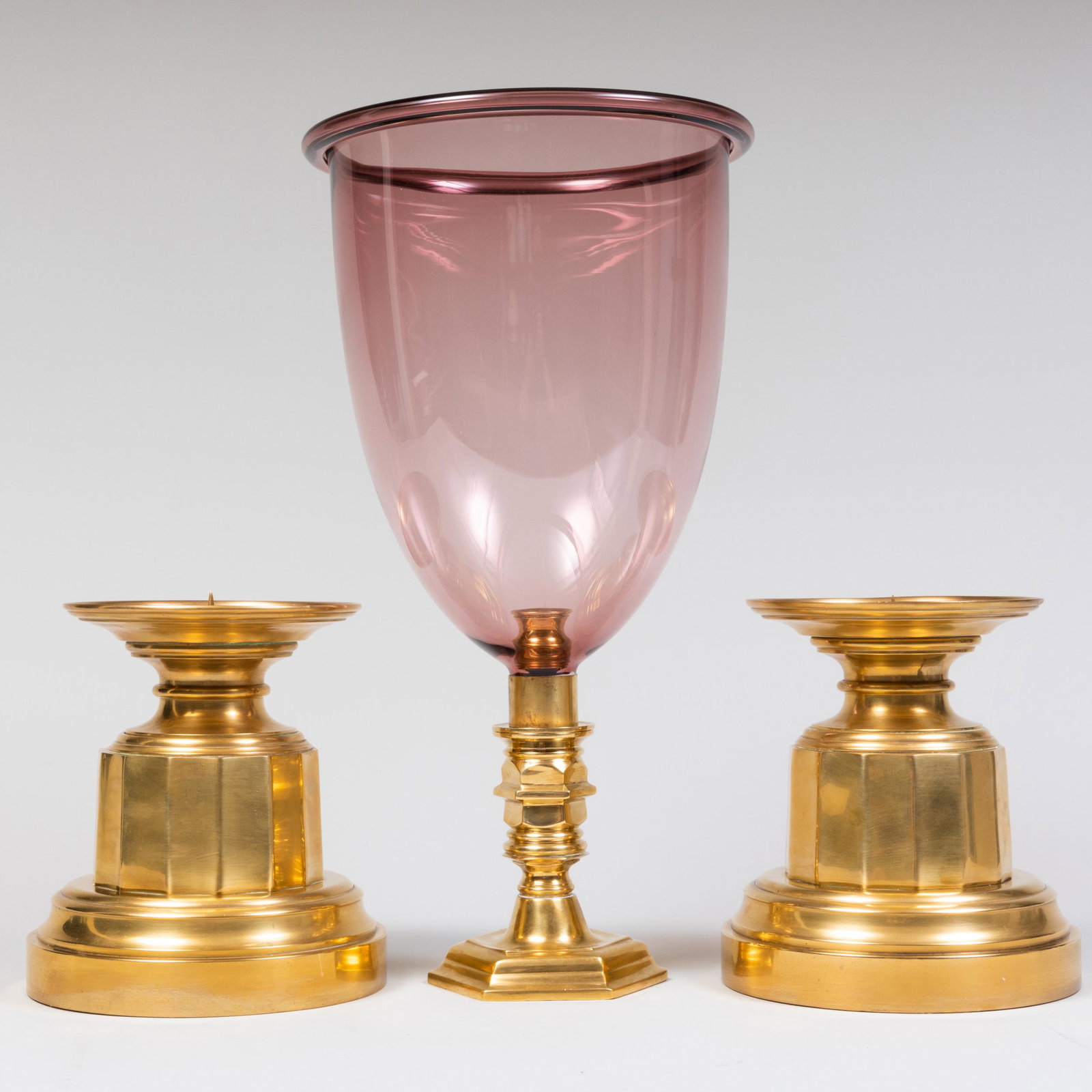 Pair of Brass Candle Holders and an Amethyst Glass Photophore: Pair of Brass Candle Holders and an Amethyst Glass Photophore The pair 9 x 8 1/4 in. diam., the photophore 18 1/2 x 10 1/2 in. diam. Property from the Collection of Susan Lasker Brody