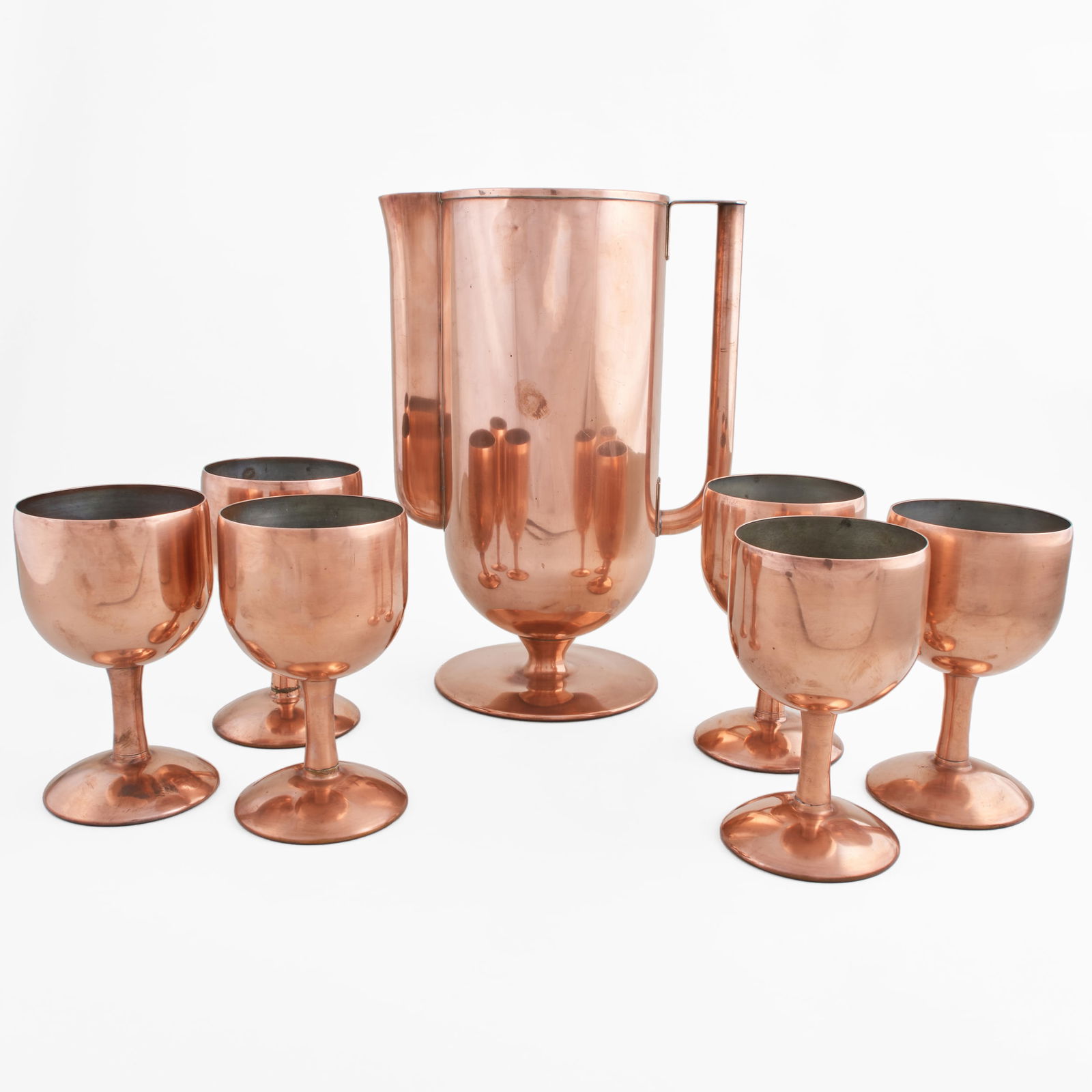 Norman Bel Geddes for Revere Copper Drinkware Set: Norman Bel Geddes for Revere Copper Drinkware Set Unmarked. Comprising: A pitcher Six goblets The pitcher 12 x 8 3/4 x 5 3/4 in., the goblets 6 x 3 1/2 in. diam., (7 pcs).