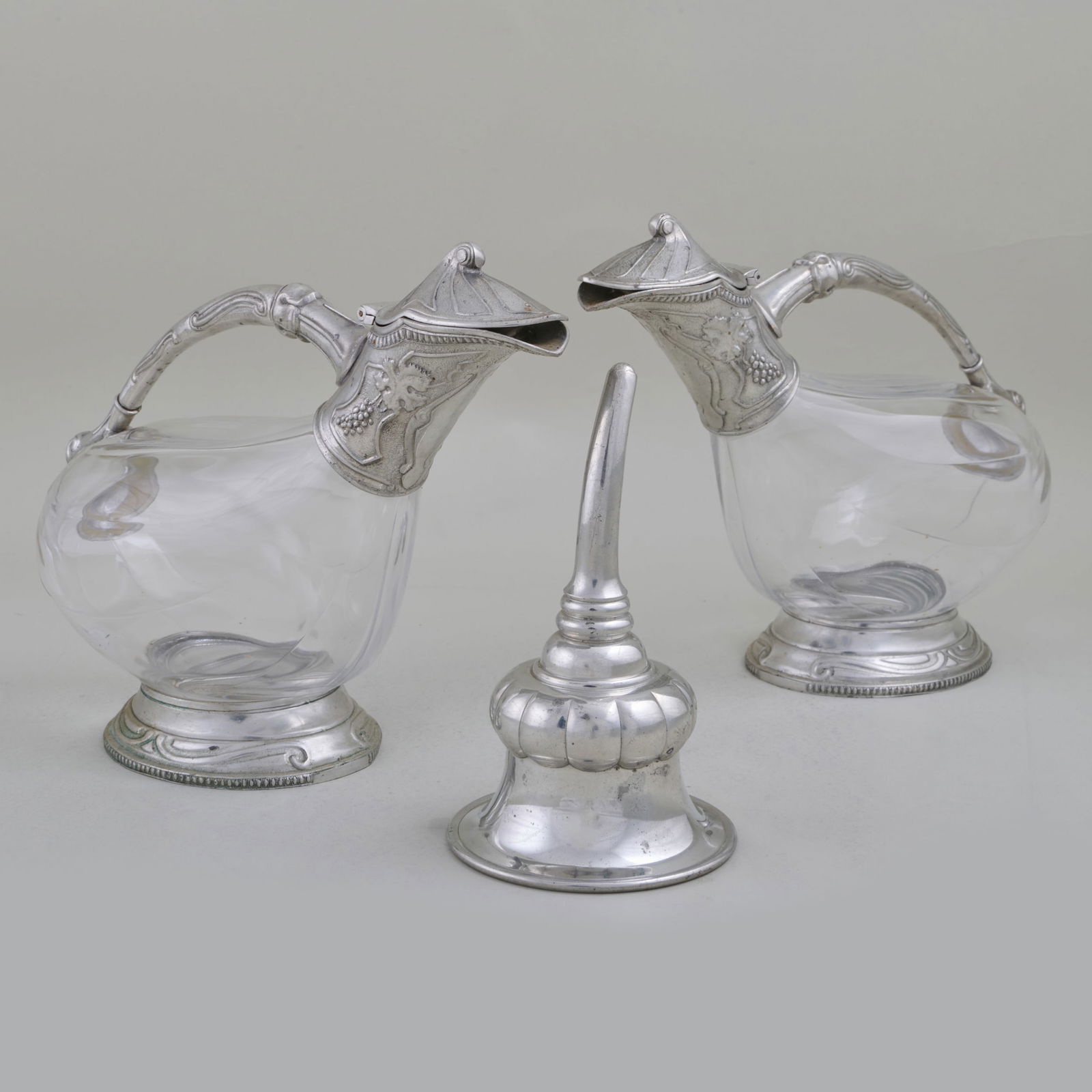 Pair of Metal Mounted Glass Decanters and a Wine Funnel: Pair of Metal Mounted Glass Decanters and a Wine FunnelDecanter with stamped mark.The decanters 8 1/4 x 10 1/2 x 4 1/4 in., the funnel 6 1/2 x 3 3/4 in. diam.Collection of Lynn Chase from Money Pit