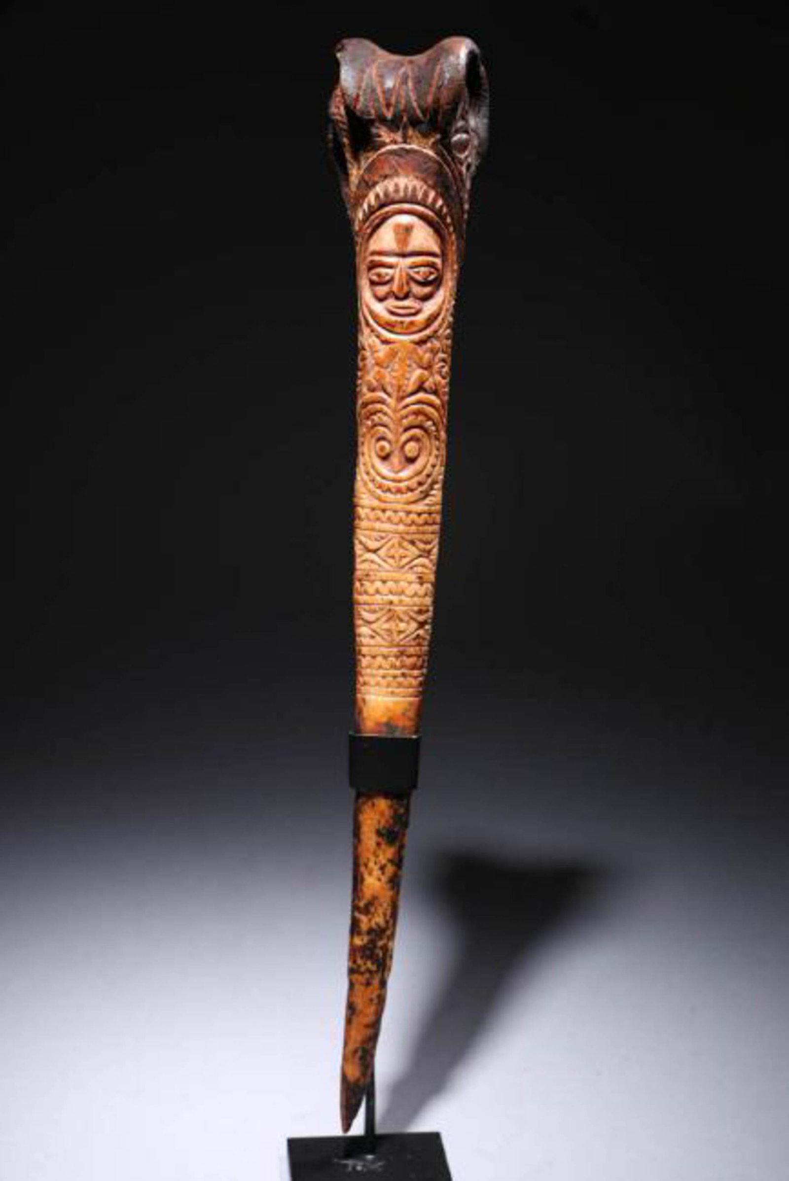 PNG Cassowary Bone Dagger: Museum quality cassowary bone dagger, incised with a face and floral design. Display stand included. Dimensions" 14" H (w/stand); Weight: 8.2 oz. w/stand. Provenance: Ex collection Julius Calabass, NY