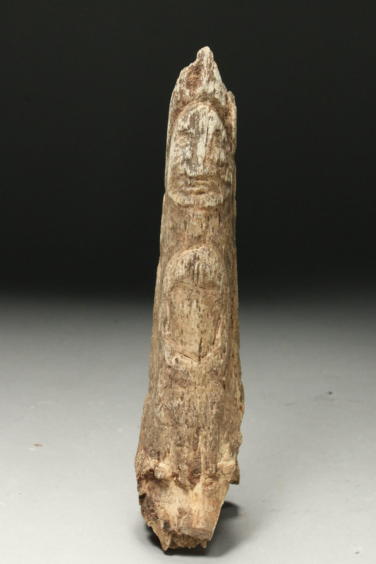 Fossilized Antler with Four Carvings: A fossilized antler section with four figures carved into the surface, two in the front and one on each side. 9" H