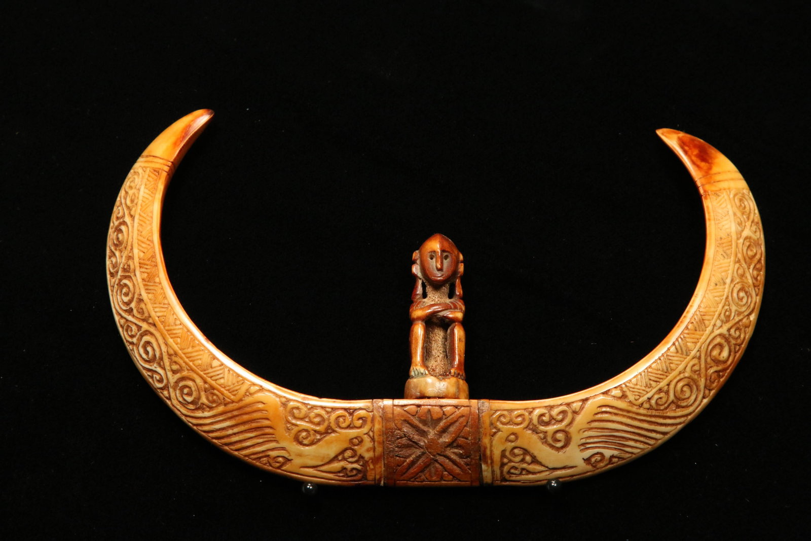 Indonesia Boar Tusk Pendant: A East Nusa Tenggara boar tusks with center figure, incised design. Wonderful honey patina. 6" W.