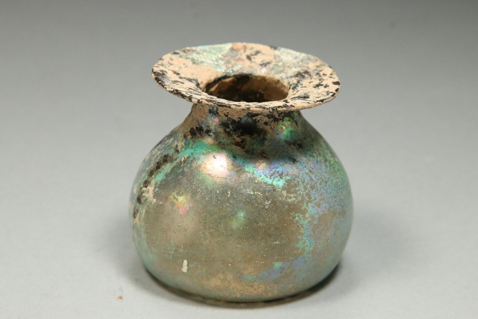 Ancient Roman Glass Jar: A beautifully iridescent green glass jar with round body, short tapered neck and wide flared rim. 2" H x 2-1/4" W Provenance: Ex collection, New York, NY