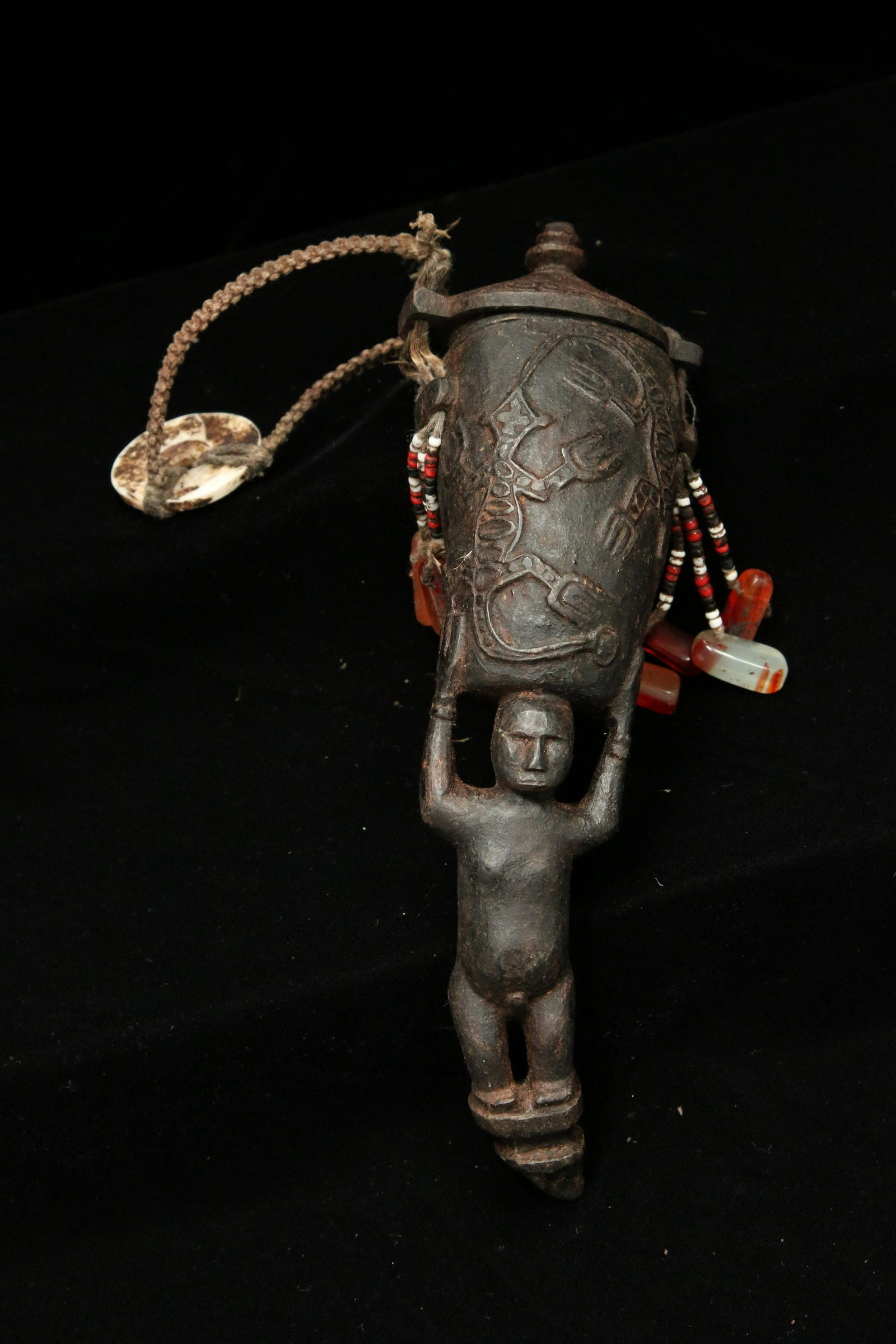 Indonesian Wood Container: An old carvedwood suspended container with carved figure holding the vessel with lizards reliefs, carved lid, old beads, fiber and bone disc. 7" H (Vessel)