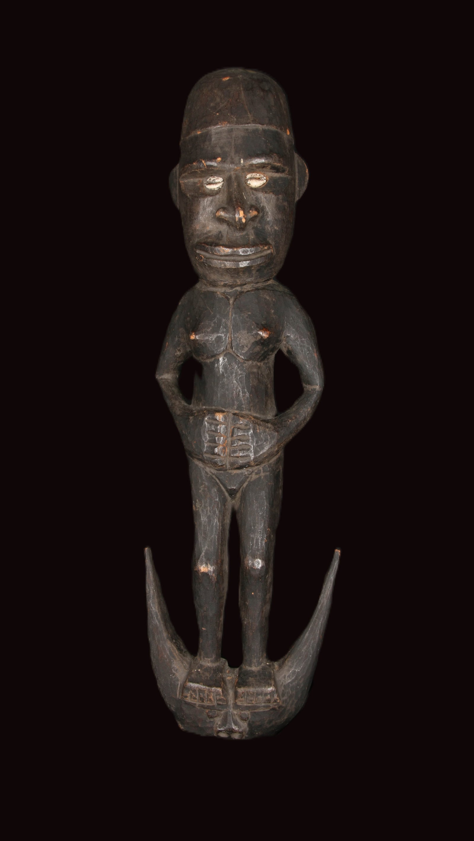 Papua New Guinea Hook Statue: A PNG Hook, called ‘‘samban’’ from Middle Sepik (PNG), with nude female figure standing upon a crescent base. Her eyes are made with cowrie shells. Dark wood with patina. The hooks are used as