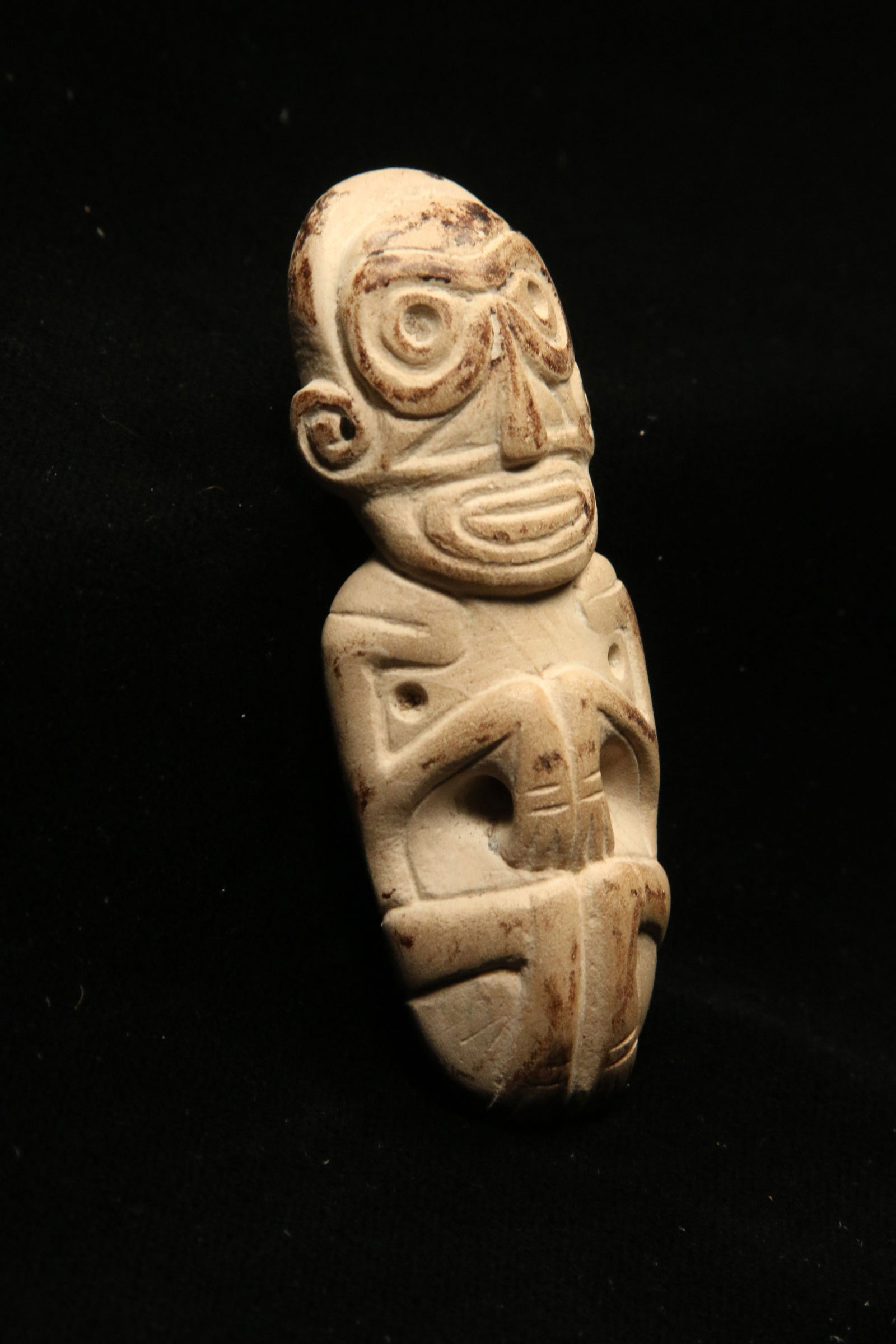 Pre-Columbian Stone Amulet: A Taino cream colored stone zemi amulet with arms bend on chest, legs folded up, broad head, with spiral pattern on reverse, and detailed bone structure. 3" L. Provenance: Ex collection Tony Milton, N