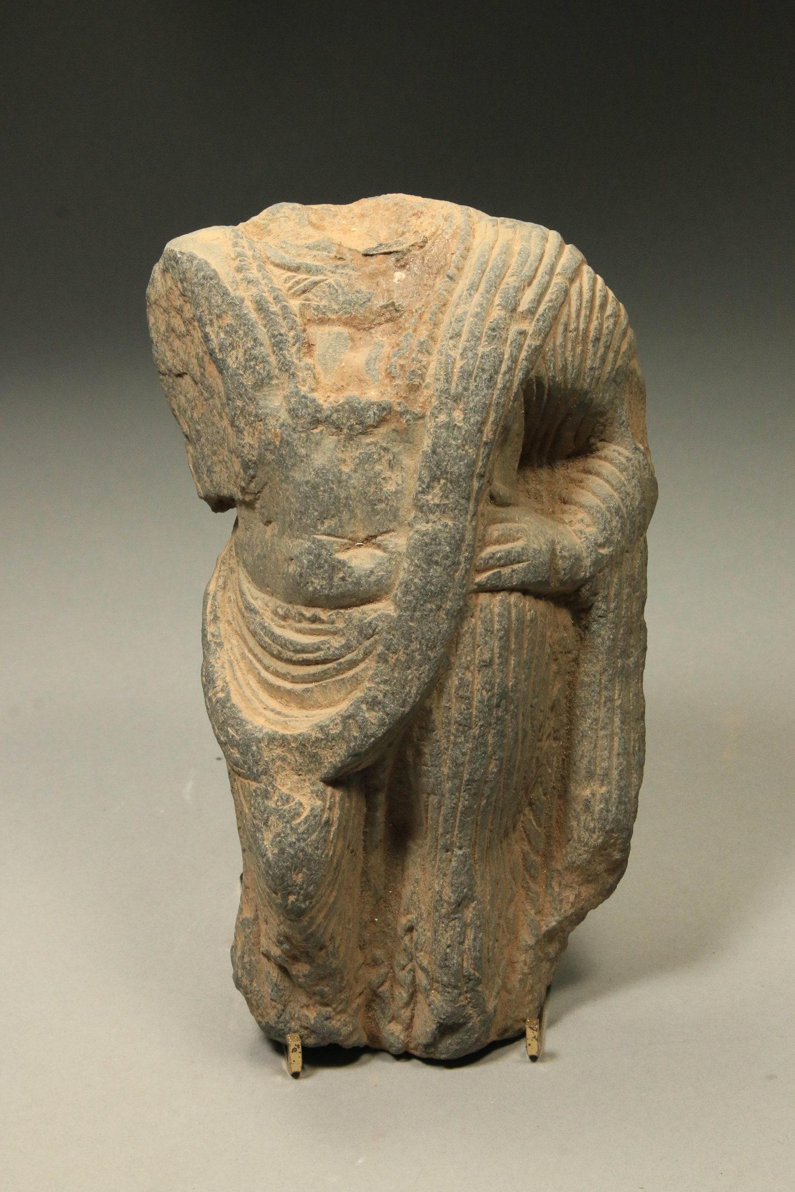 Gandharan Stone Torso: A Gandharan grey schist carved torso, wearing a robe, hand raised to waist. 9" H