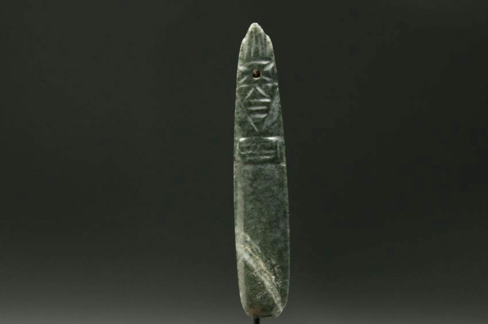 Pre-Columbian Jadeite Stone Pendant: A dark green jadeite stone celt, with tall feathered headdress. Suspension hole. 4-3/8" H Display stand included. Provenance: Ex Midwest collection.