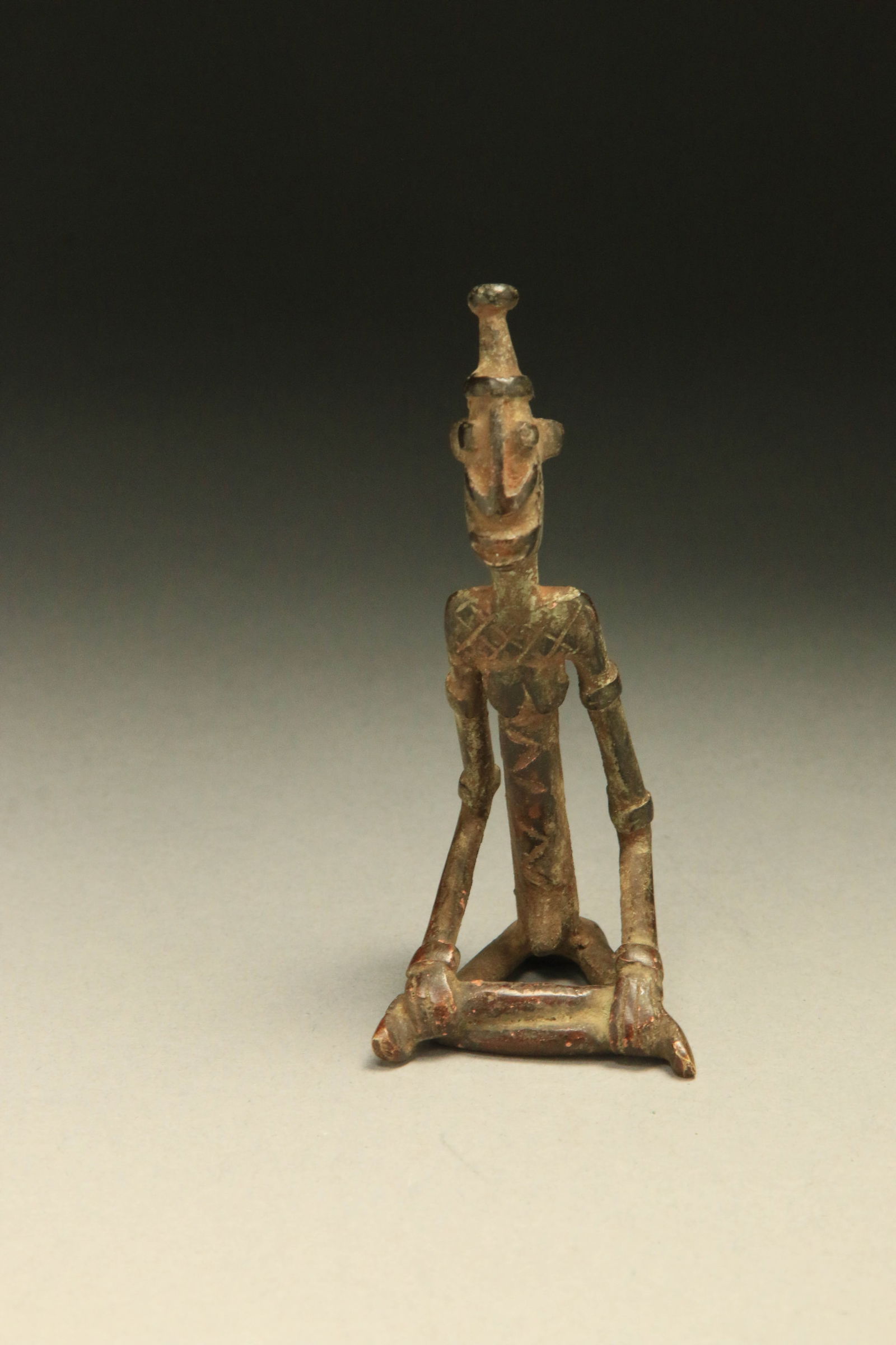 African Art Dogon Bronze Figure: A seated Dogon bronze figure wearing a hat with classic Dogon facial features. 3-3/4" H. Provenance: Ex. Collection P. Gould, NYC.
