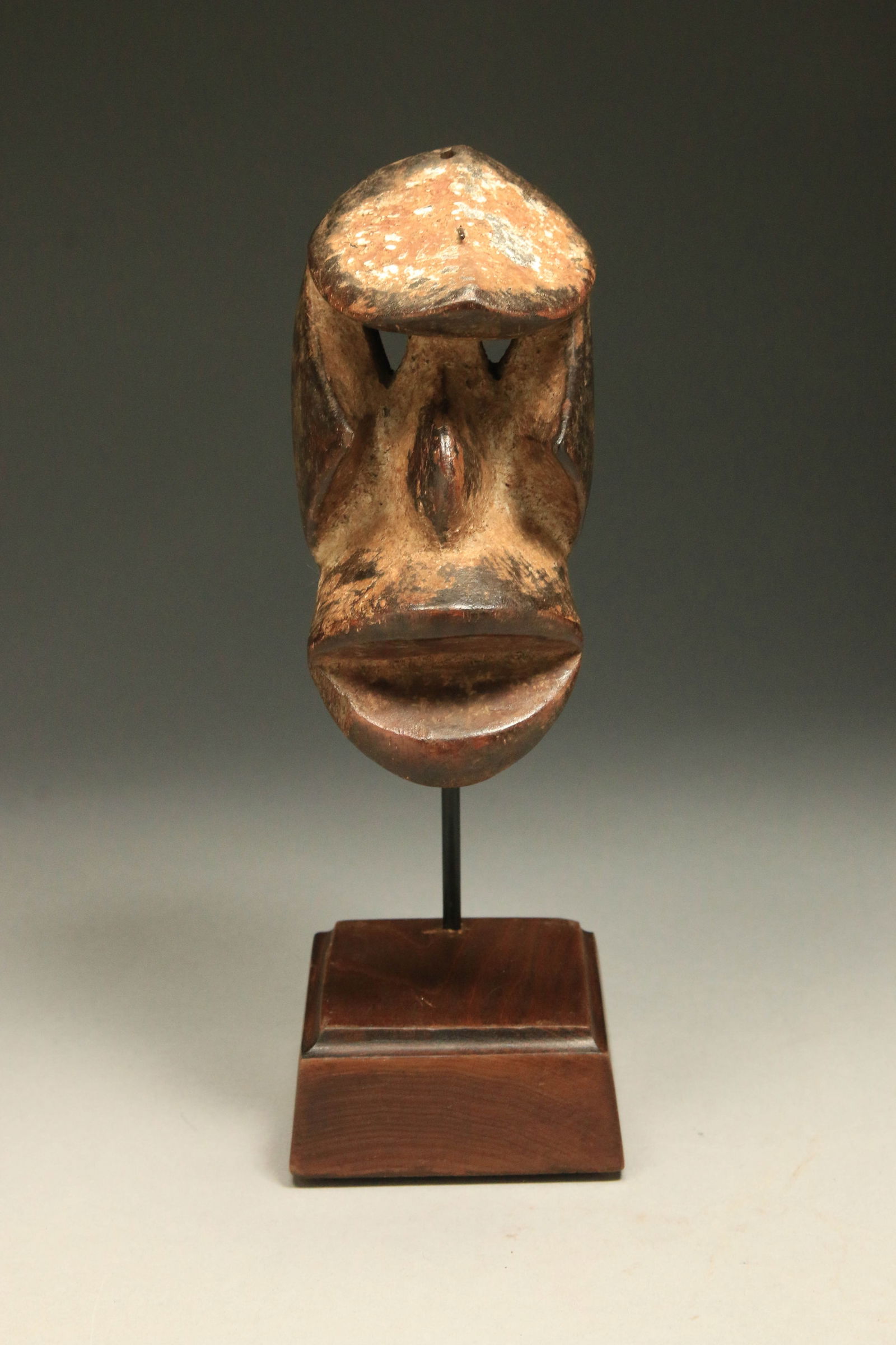 African Art Dan Passport Mask: A We Dan wood passport mask with recessed eyes, with angular checks, strong projected mouth. Great patina, nail protruding from top of the head. Display stand is included. 6" H. Provenance: Ex collect