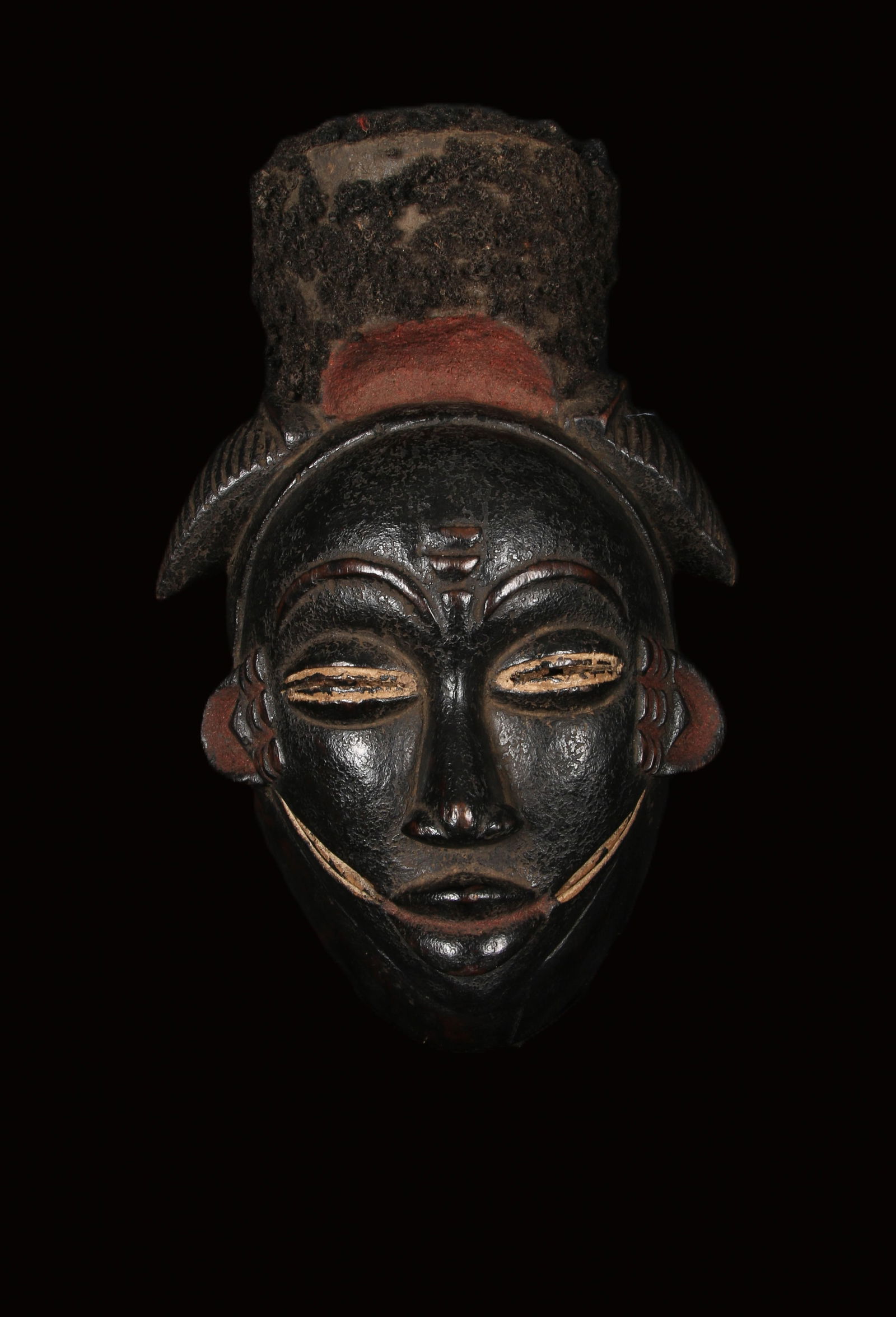African Art Blackened Punu Mask: A Punu Ikwara Mask, Gabon. Wood mask with a tower headdress and glued hair. Scarification on forehead, white highlighted eye, red highlights at bottom of hair, ears and mouth. 12" H. Provenance: Ex. c