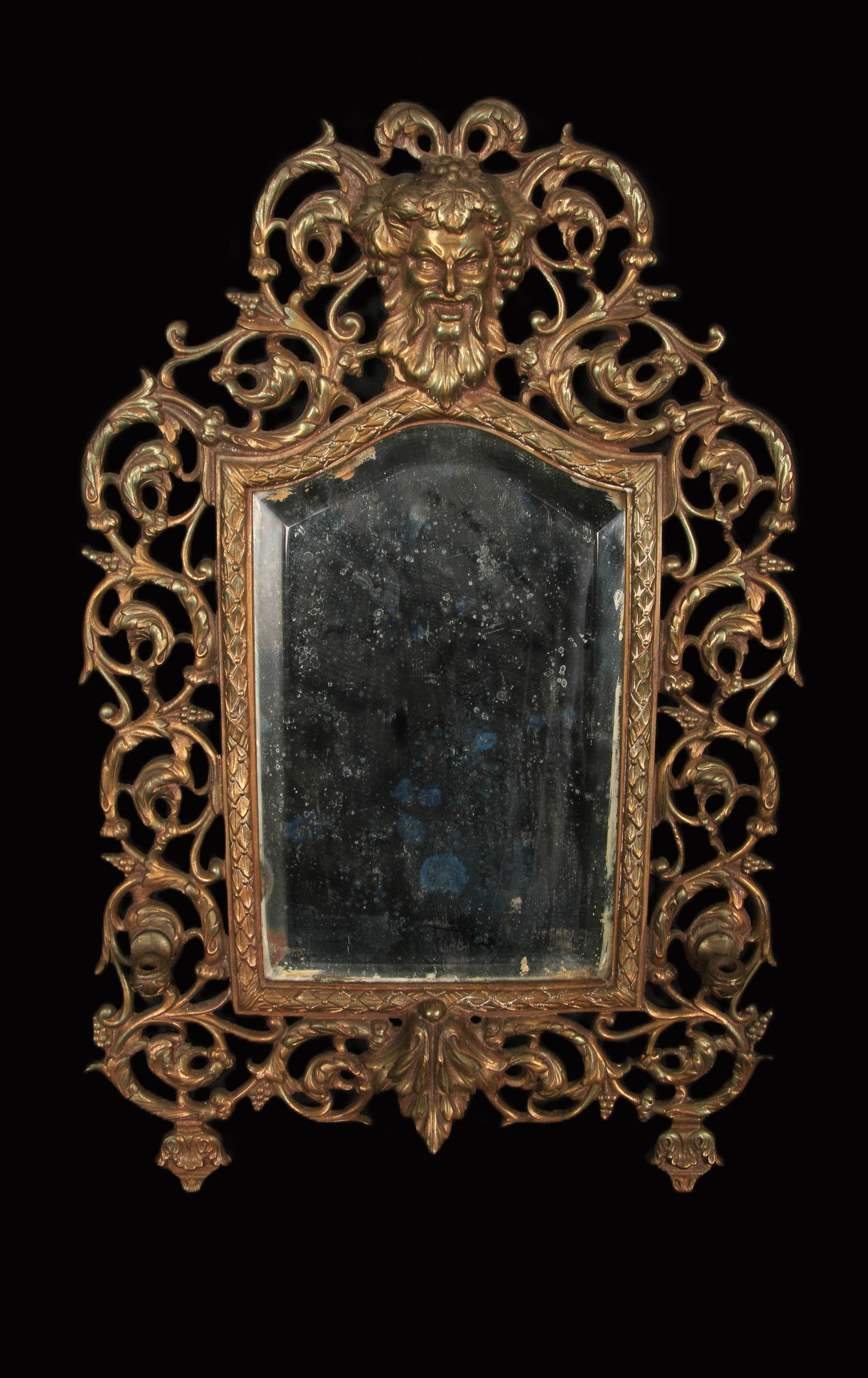 Antique Gilt Bronze Mirror: A 19th century gilt bronze mirror with rococo scroll work, acanthus leaves and featuring Bacchus with beard and grapes. Candle stick holders on either side of the mirror. Foundry marked on reverse "P.