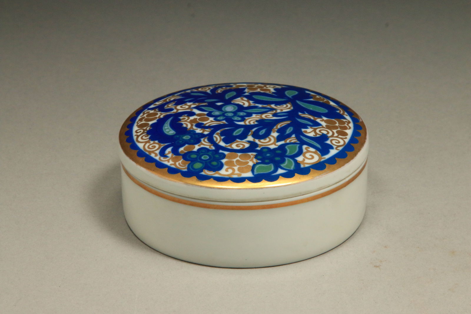 Rosenthal Porcelain Trinket Box: Rosenthal porcelain trinket box with a blue, green, and gold floral pattern, made in Germany. Art Deco floral design. Marked on reverse of lid and reverse of base. 4" L x 1-1/2" H.
