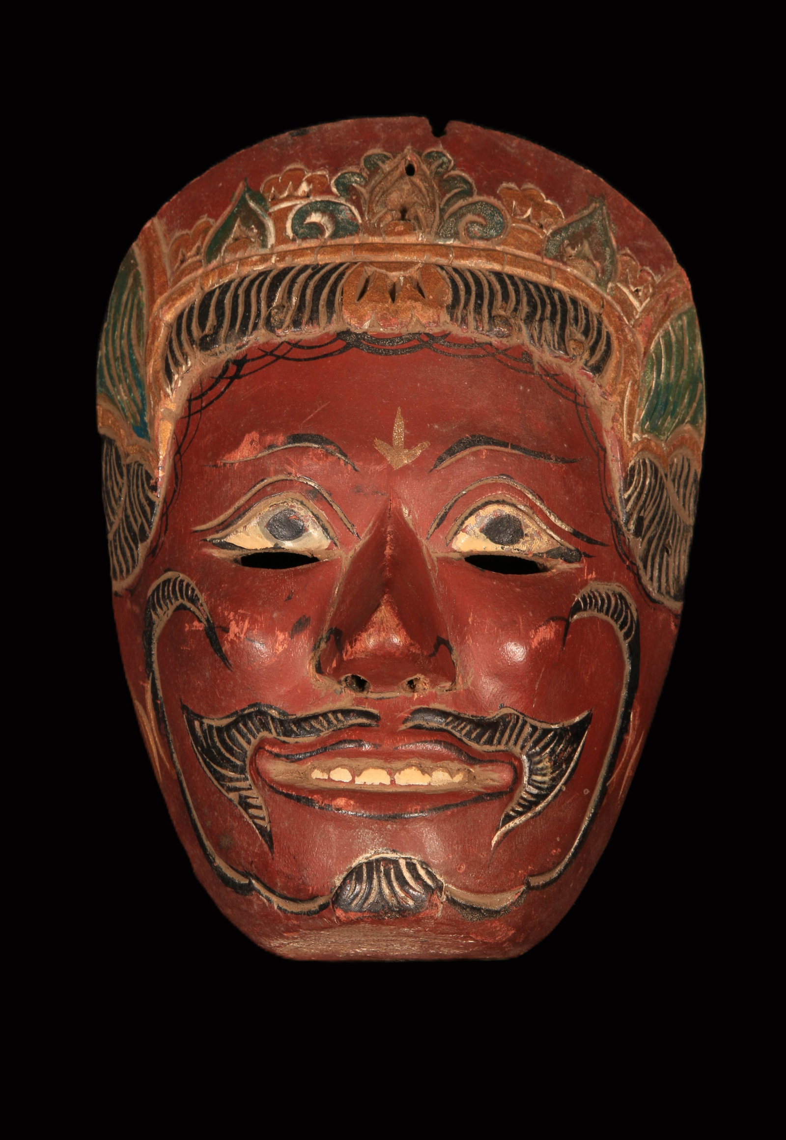 Indonesia Wayang Topeng Mask: A Javanese Wayang Topeng mask, hand-carved wood finished with polychrome paint and wearing a stylized crown. The red face with black detailing typically indicates characters that are powerful, aggress