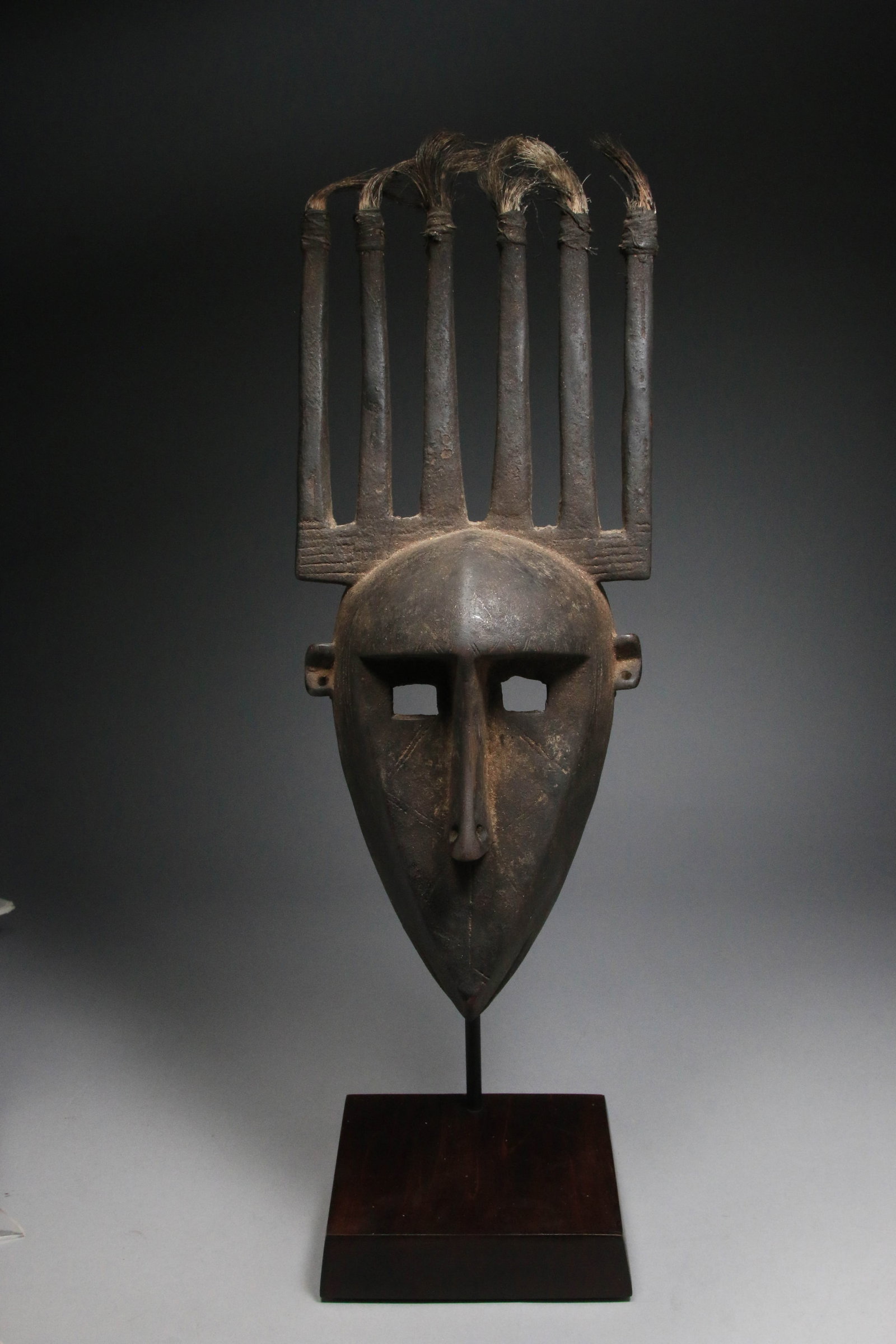 African Art Minaka Mask - Bamana People: A N'tomo (or Ndomo) initiation mask from the Bamana (Bambara) people of Mali. Oval shape face with pointed chin, delicate mouth. Six feathered horns on top of head. 17" L. Display stand is included. P