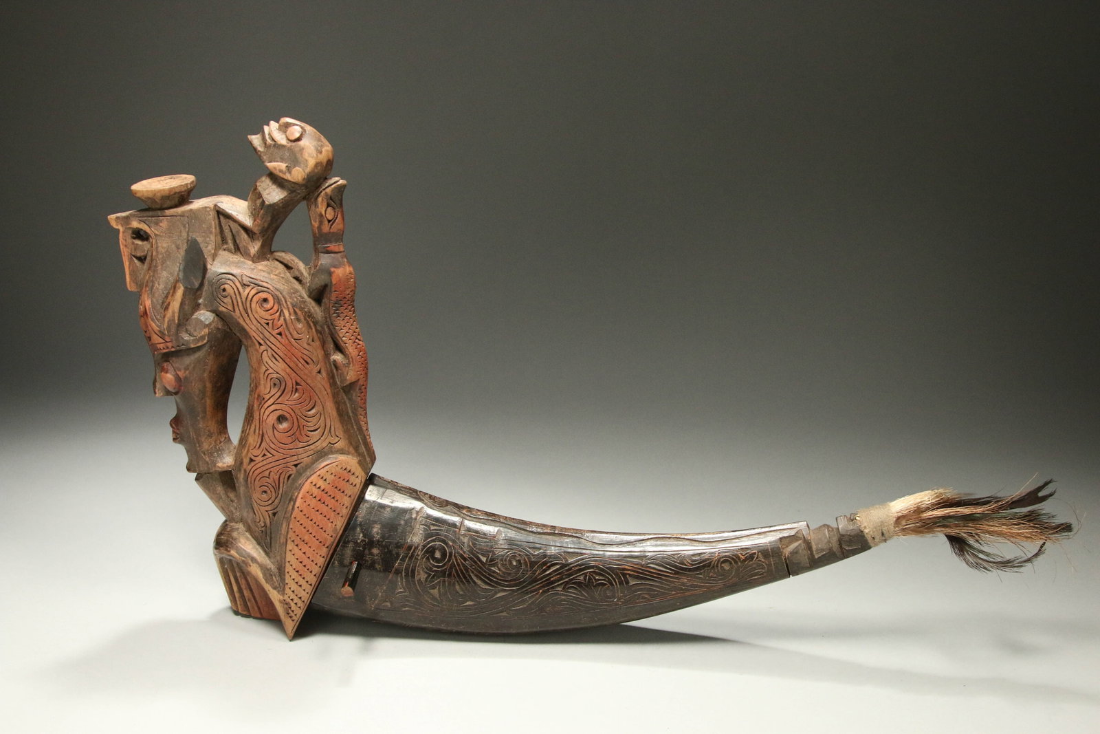 Indonesian Wood and Horn Medicine Container: A large wood and horn herbal medicine container with sea animal finial, with rider and lizard. Horn container, finely incised with feathered figure at end of tail. 20" L